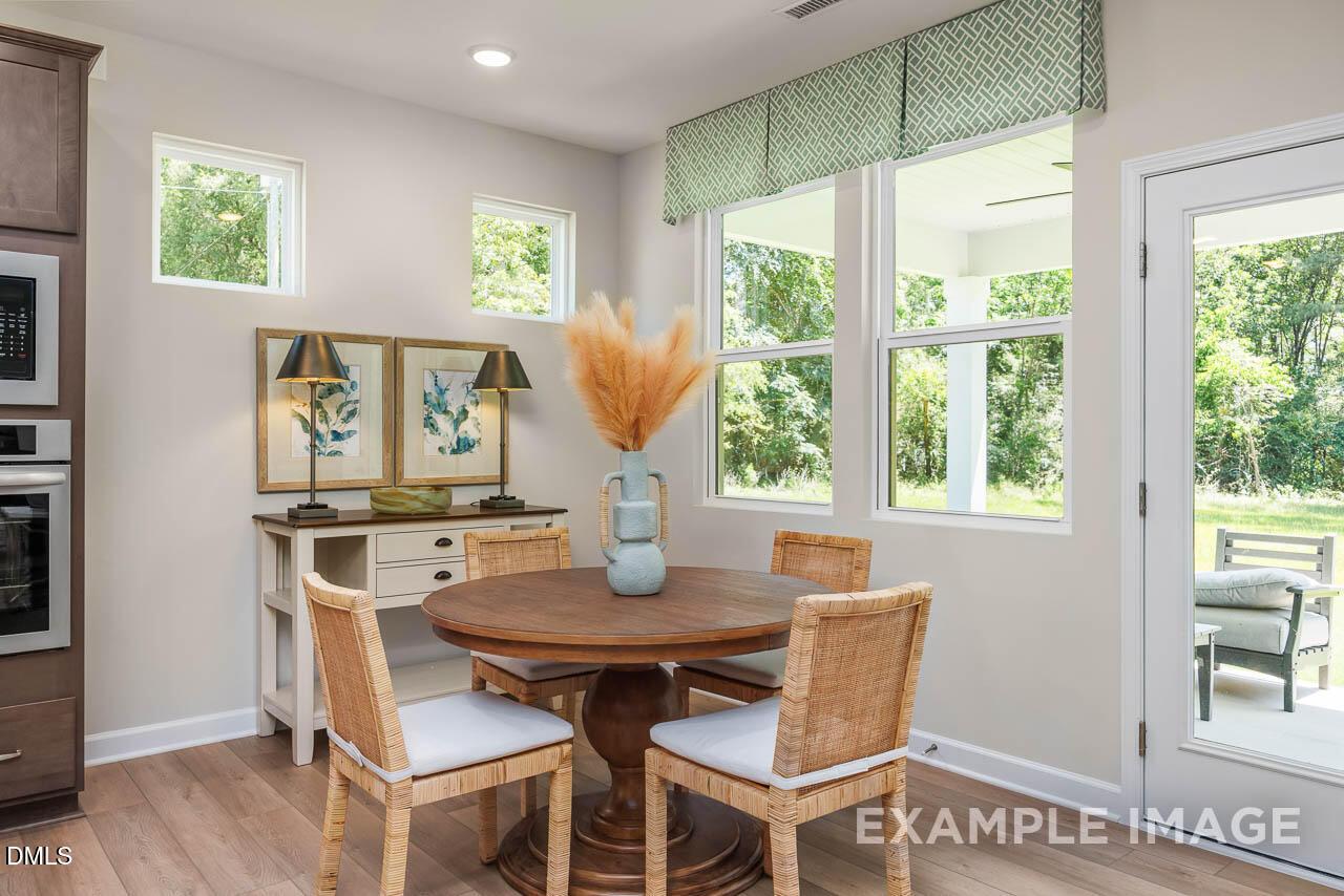 Bright dining room with round wooden table, wicker chairs, and pampas grass overlooking wooded backyard in The Willow B, Wake Forest