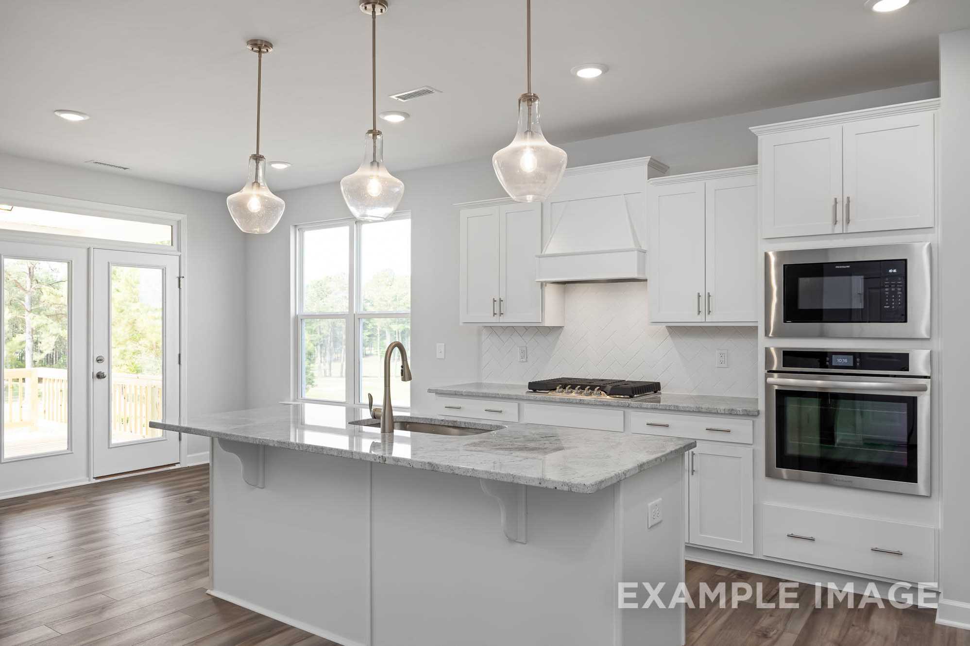 Spacious kitchen in The Ash Davidson Homes design with white shaker cabinets, quartz island, stainless steel double ovens, and pendant lighting