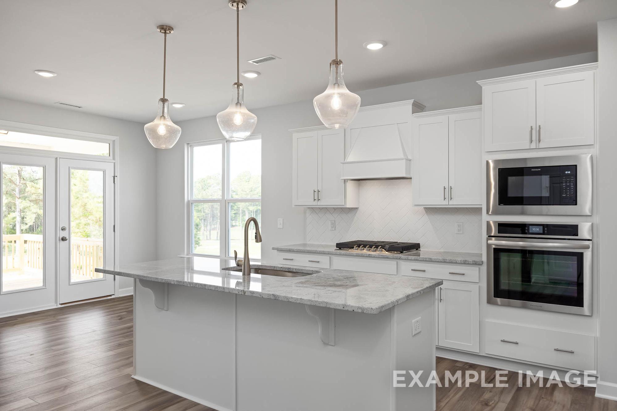 Spacious kitchen in The Ash Davidson Homes design with white shaker cabinets, quartz island, stainless steel double ovens, and pendant lighting