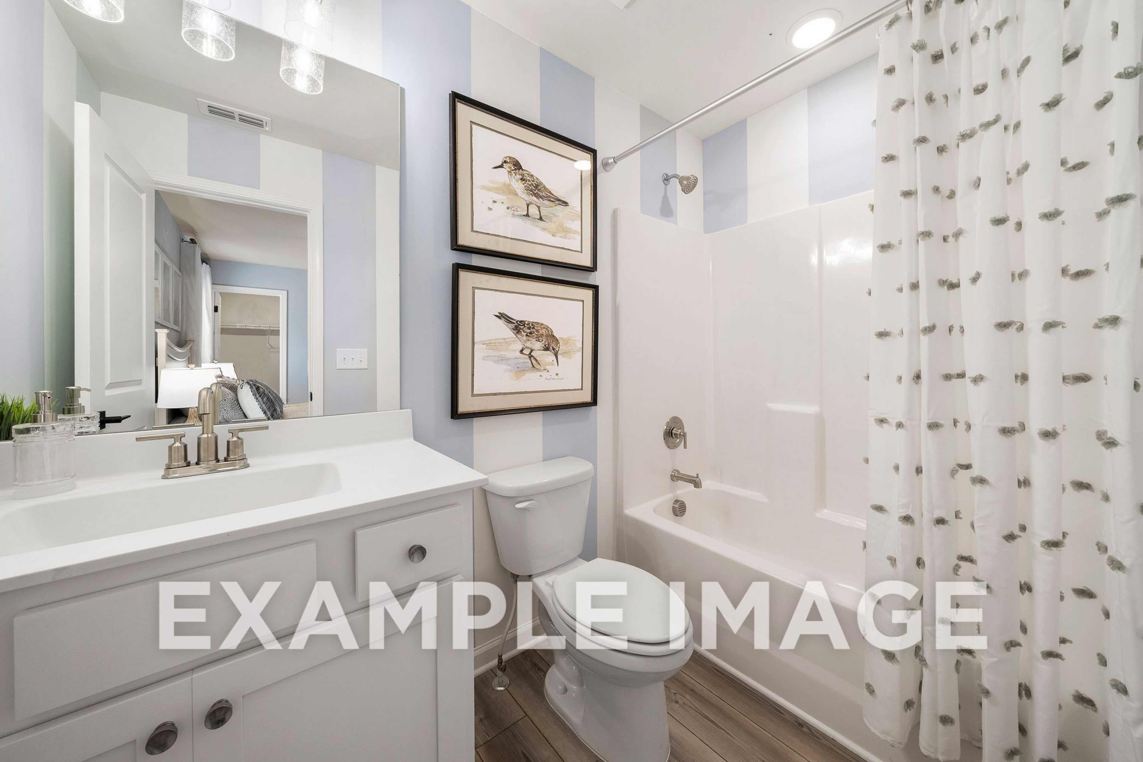 Bright bathroom in The Hickory A with blue striped walls, white vanity, soaking tub, and bird artwork