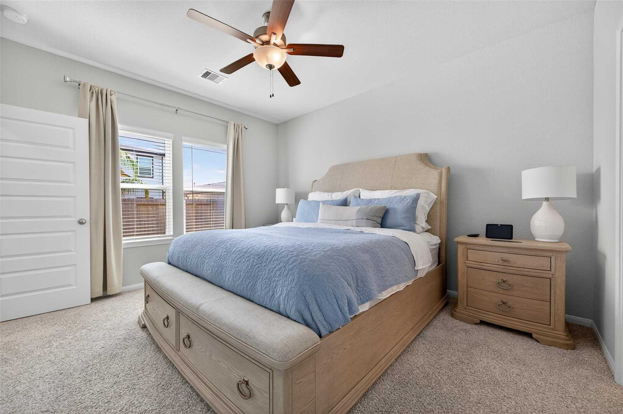 Cozy secondary bedroom with upholstered storage bed, blue bedding, ceiling fan, and window in Davidson Homes The Brazos E, Magnolia, Texas