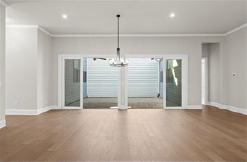 Spacious living room with light hardwood floors, chandelier, and sliding doors to covered patio in Davidson Homes The Seaside A, Woodstock, GA