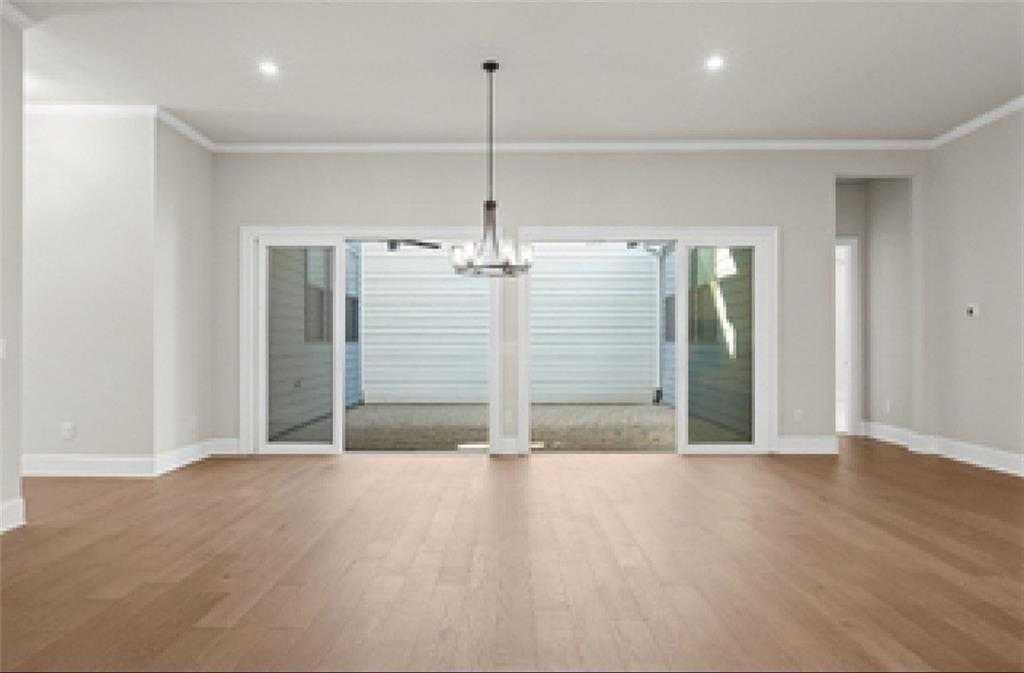 Spacious living room with light hardwood floors, chandelier, and sliding doors to covered patio in Davidson Homes The Seaside A, Woodstock, GA