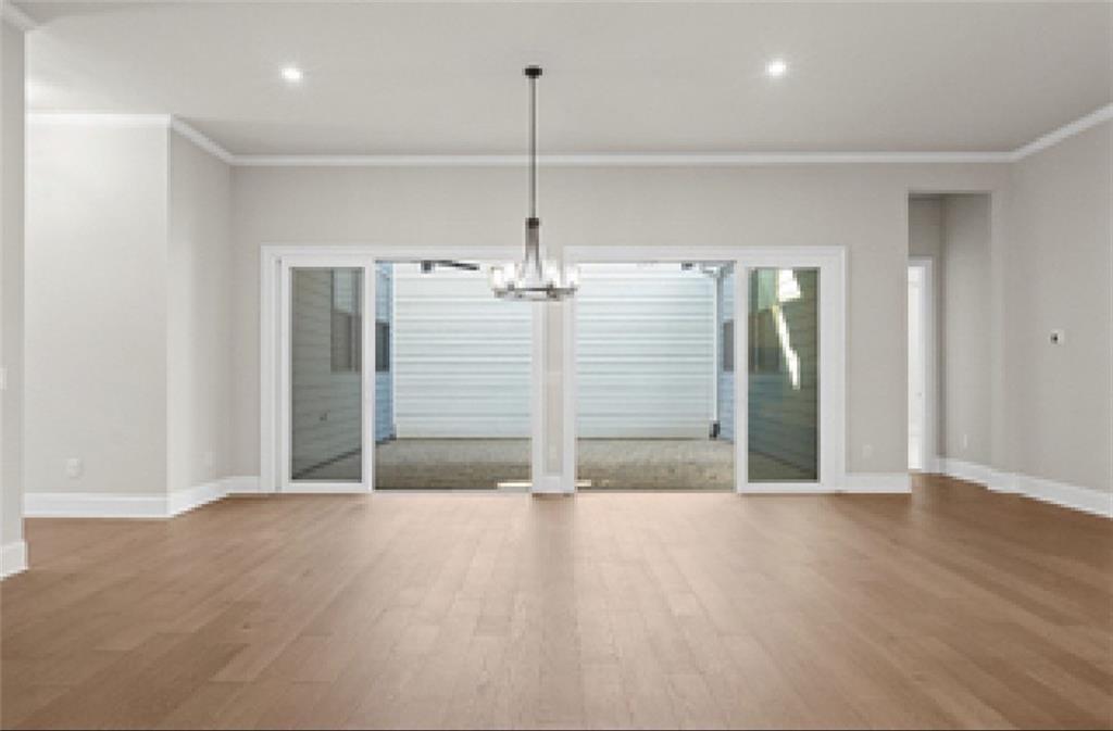 Spacious living room with light hardwood floors, chandelier, and sliding doors to covered patio in Davidson Homes The Seaside A, Woodstock, GA