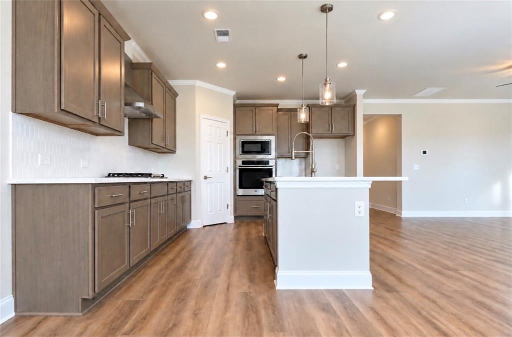 Open-concept kitchen with gray cabinets, white island, and hardwood floors in The Harrison H plan, Wehunt Meadows, Hoschton, GA
