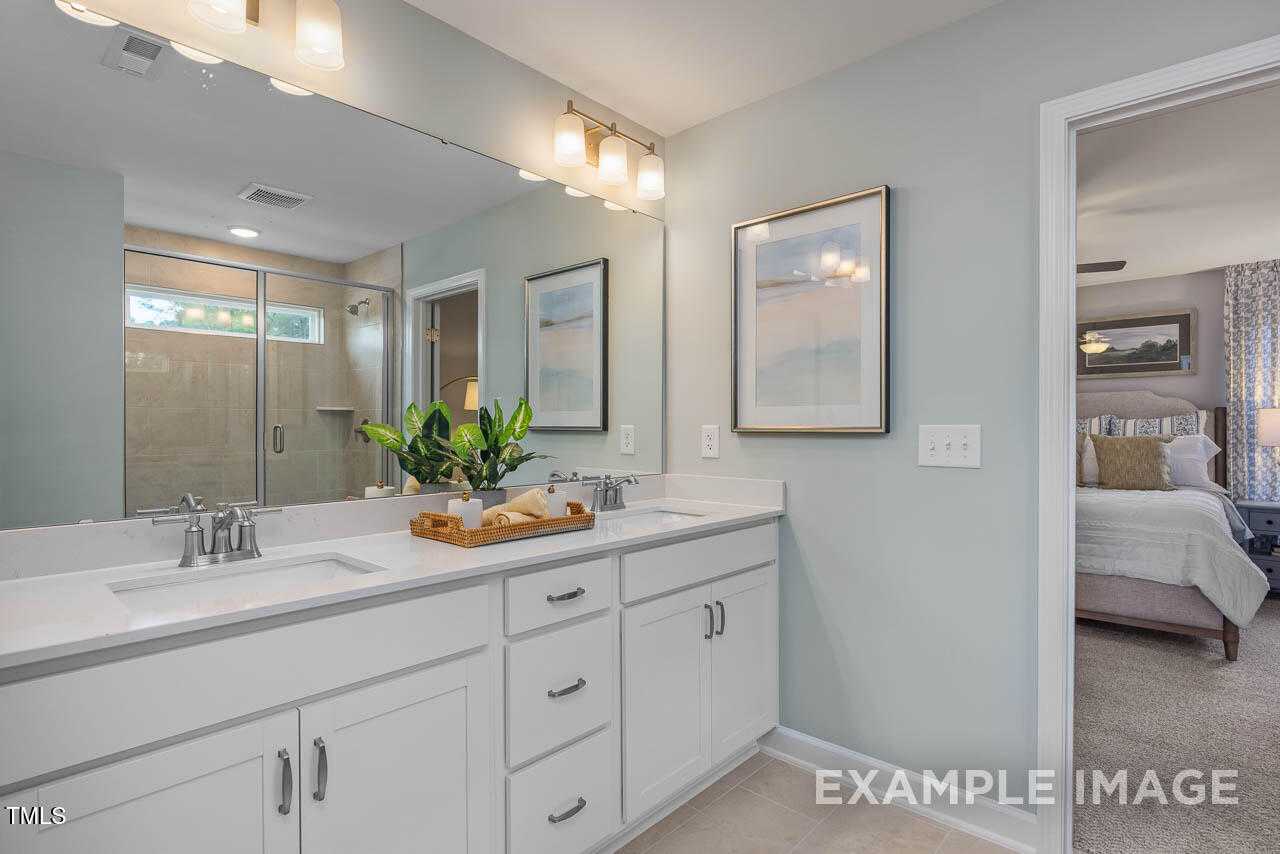 Elegant master bathroom with white double vanity, glass shower, and adjacent bedroom suite in Davidson Homes The Willow G, Angier, NC