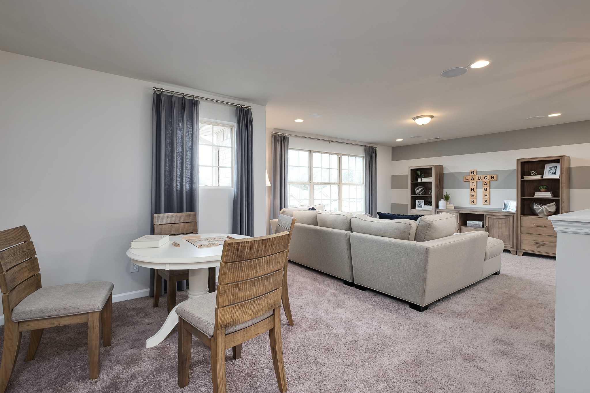 Open-concept dining and living area at The Reserve at Overton in Hampton Cove, Alabama with round wooden table, gray sectional sofa, and large windows