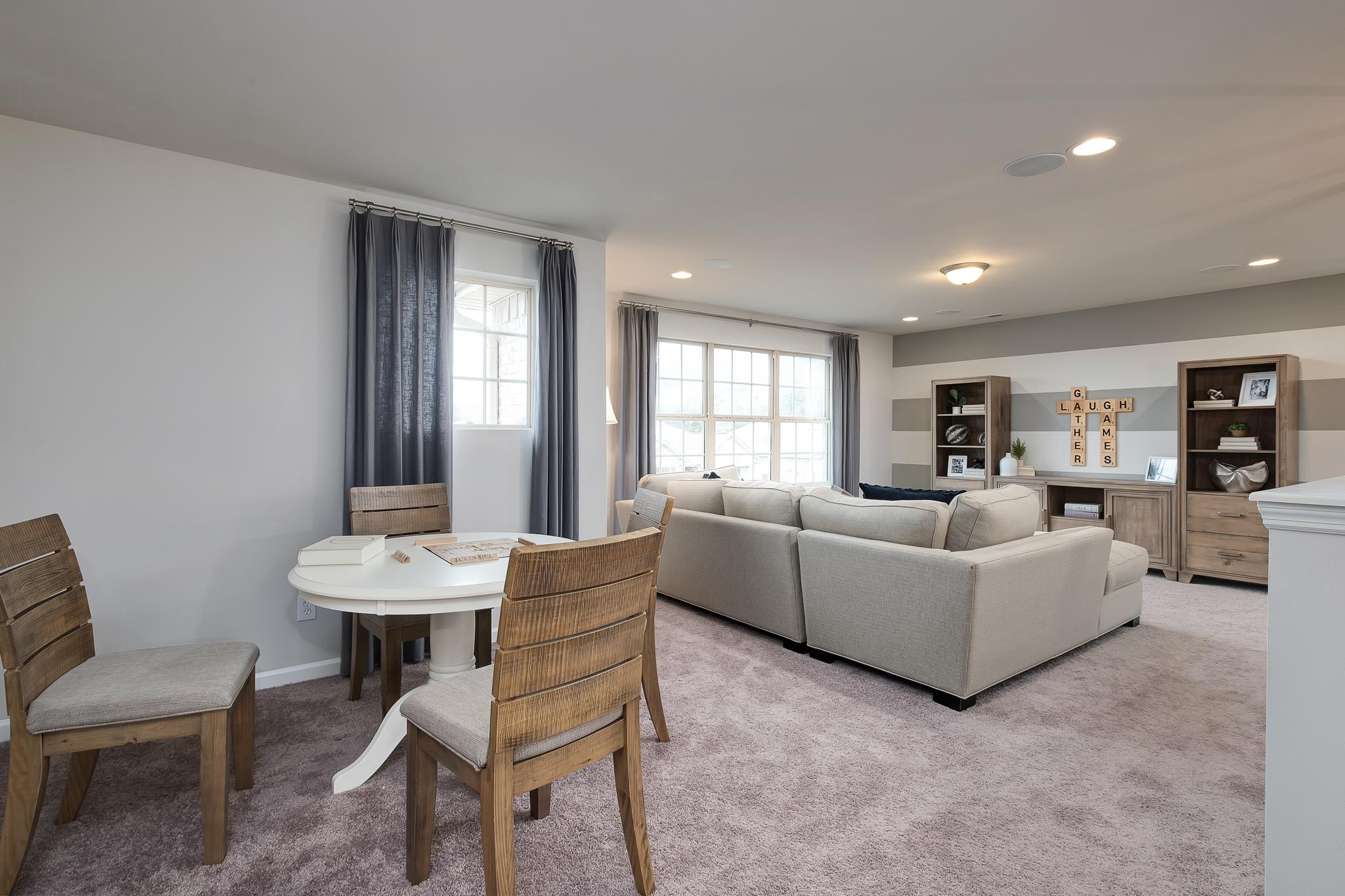 Open-concept dining and living area at The Reserve at Overton in Hampton Cove, Alabama with round wooden table, gray sectional sofa, and large windows