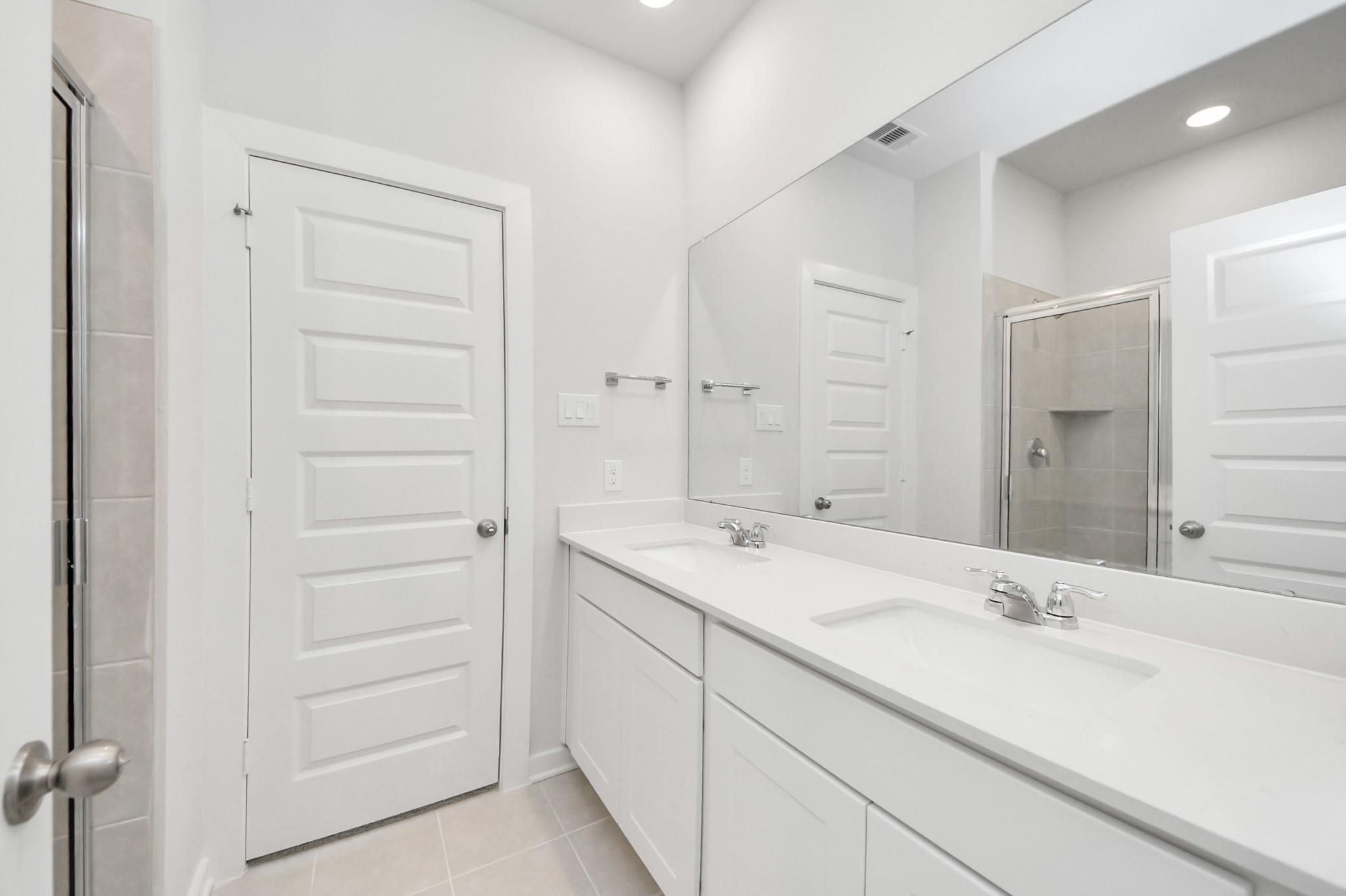 Modern primary bathroom with double vanity, white cabinets, and large mirror in The Frio F floor plan, Cleveland, Texas.