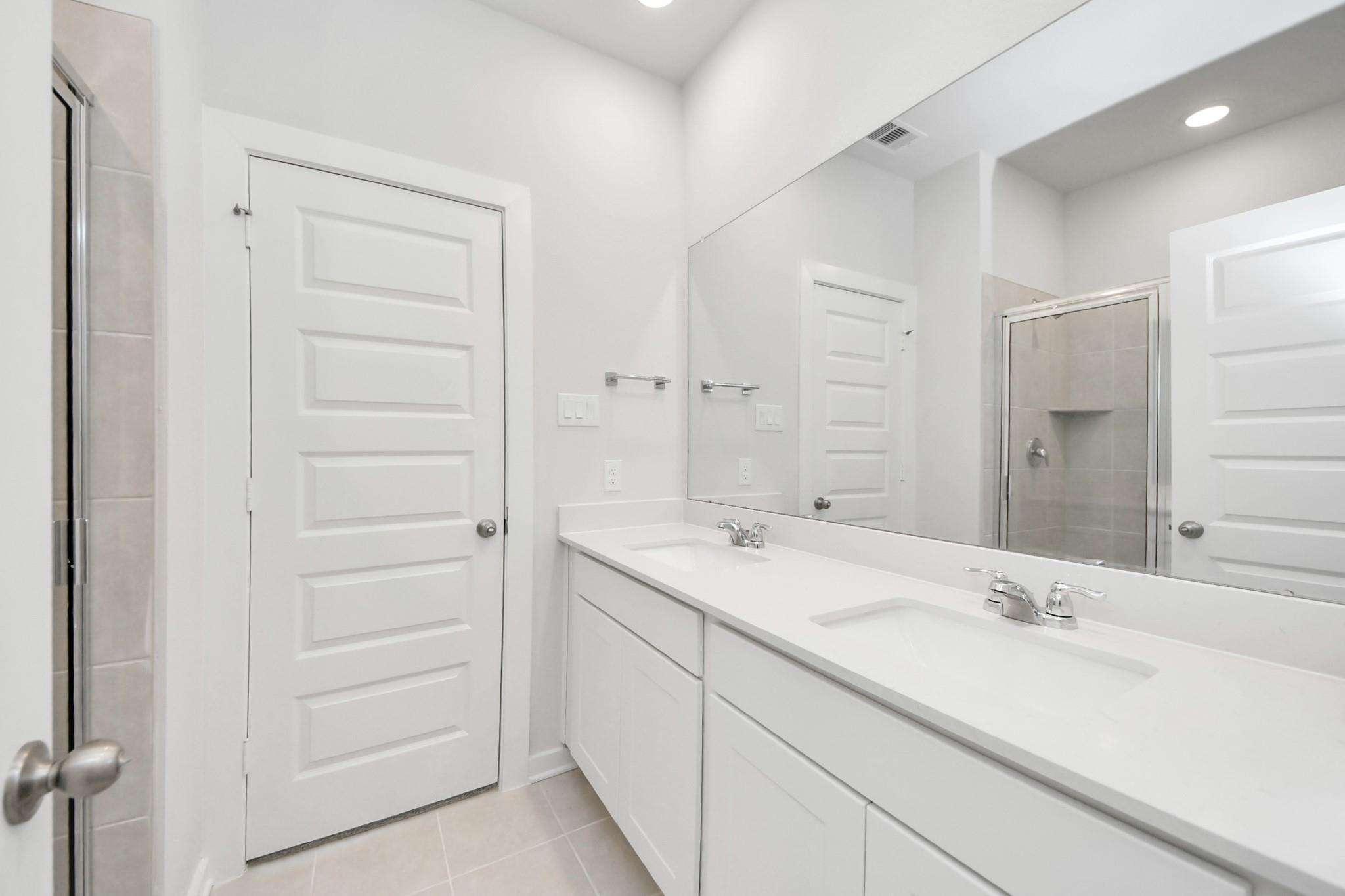 Modern primary bathroom with double vanity, white cabinets, and large mirror in The Frio F floor plan, Cleveland, Texas.