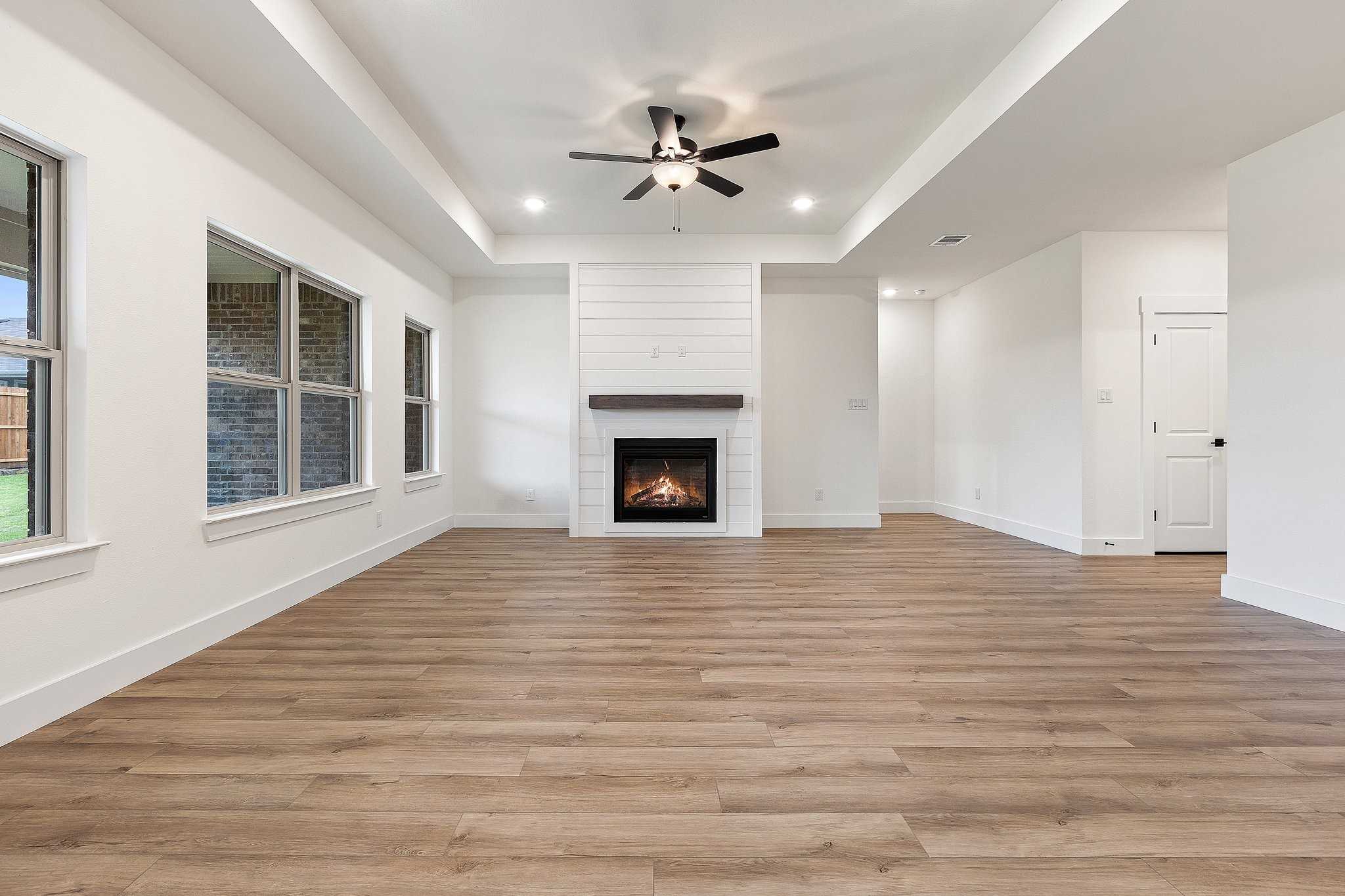 Spacious living room with shiplap fireplace, hardwood floors, and ceiling fan in Davidson Homes The Rockford C, Josephine, Texas