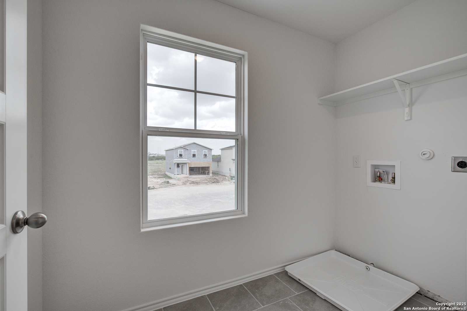 Bright laundry room with built-in shelves, washer-dryer hookups, and window view of new homes in Davidson Homes The Trinity A, San Antonio