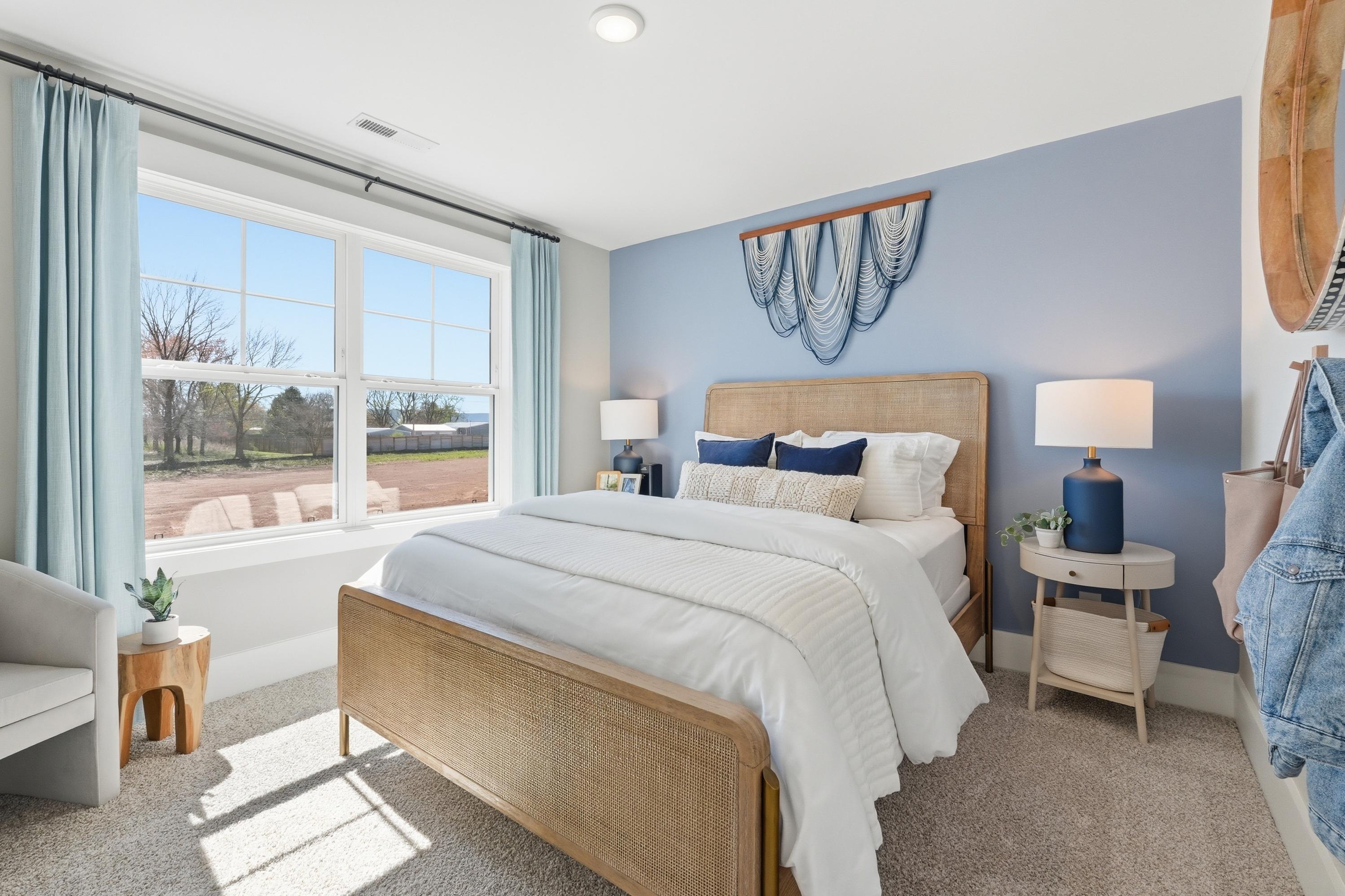 Cozy bedroom interior at Berry Cove in New Market Alabama with light blue walls rattan bed frame and large sunny window