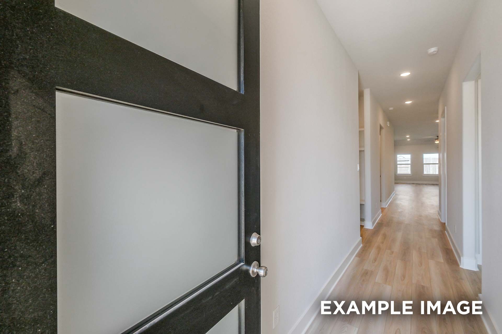 Spacious hallway in The Luna J Davidson Homes design, Katy Texas, featuring open frosted glass door, hardwood floors, recessed lights