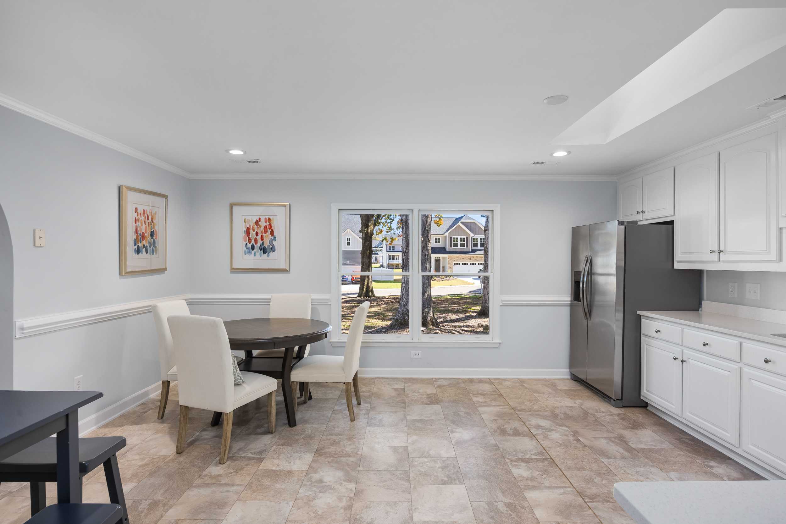 Spacious kitchen dining area in Stagecoach Corner home by Davidson Homes, Mebane NC with white cabinets, round table, and pool views