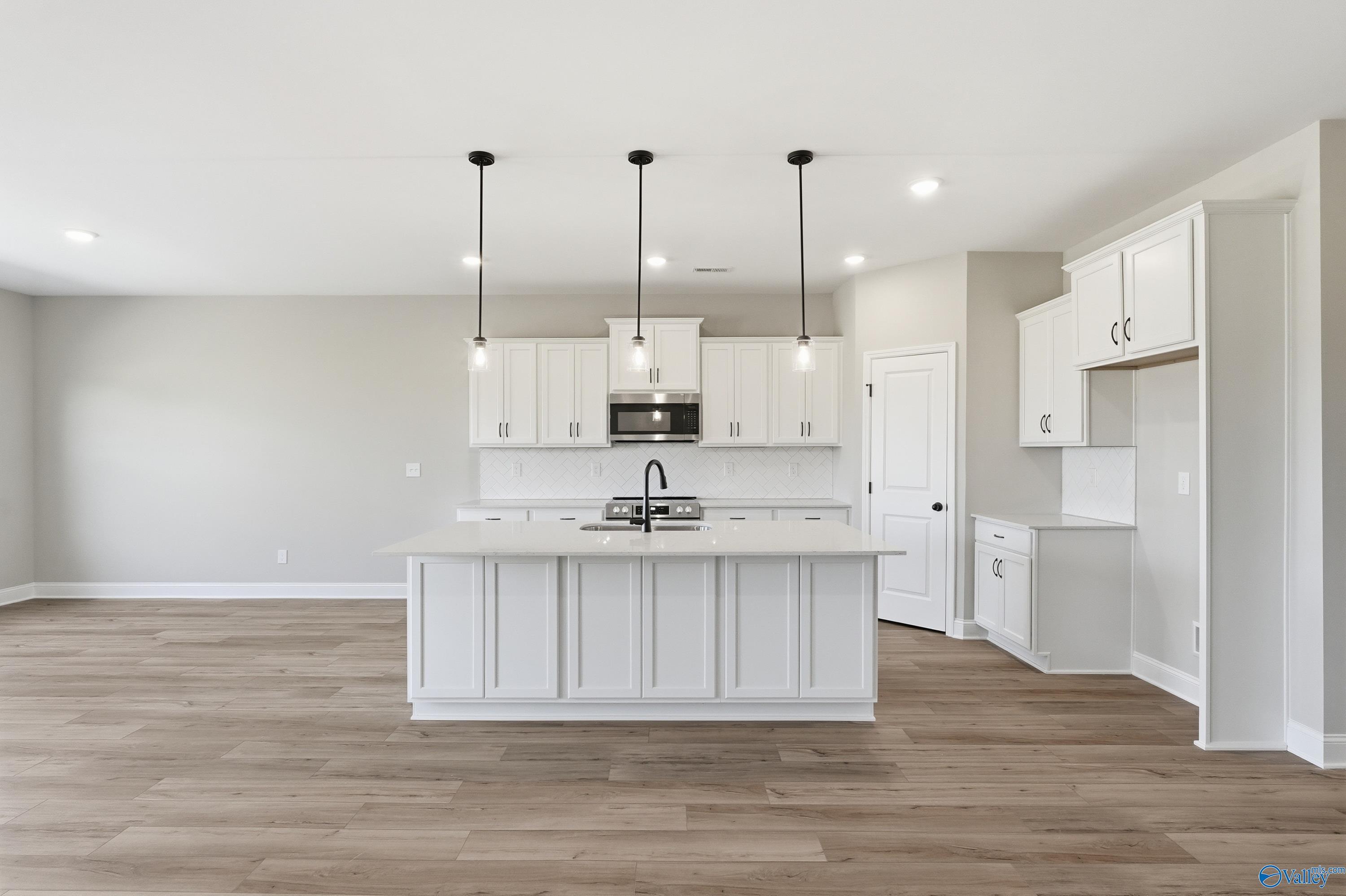 Spacious modern kitchen with white shaker cabinets, large island, pendant lights, stainless appliances in Davidson Homes The Rockford, Harvest AL