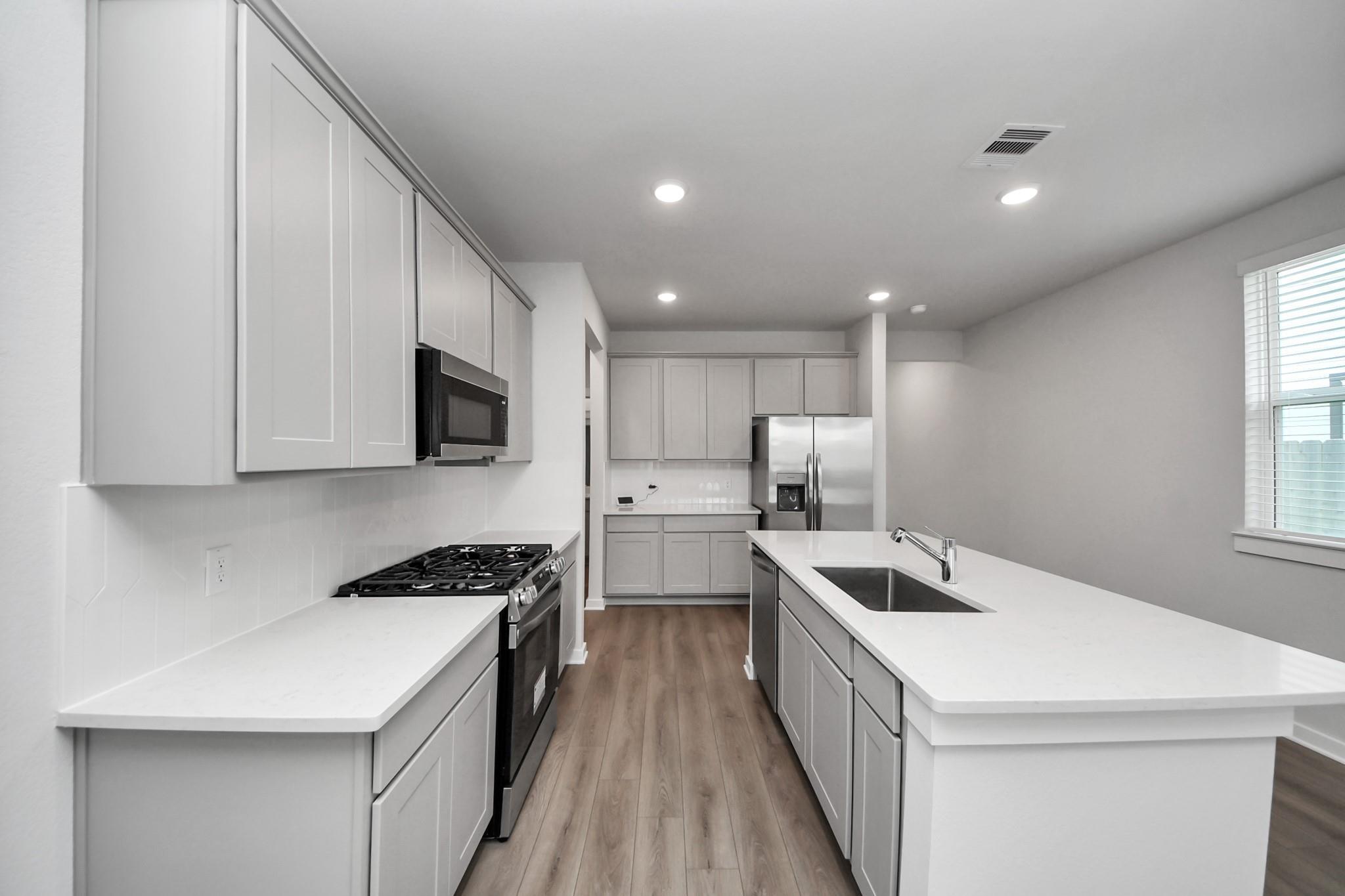 Modern kitchen with white shaker cabinets, island with sink, gas range, and stainless appliances in Davidson Homes Frio F plan, Houston