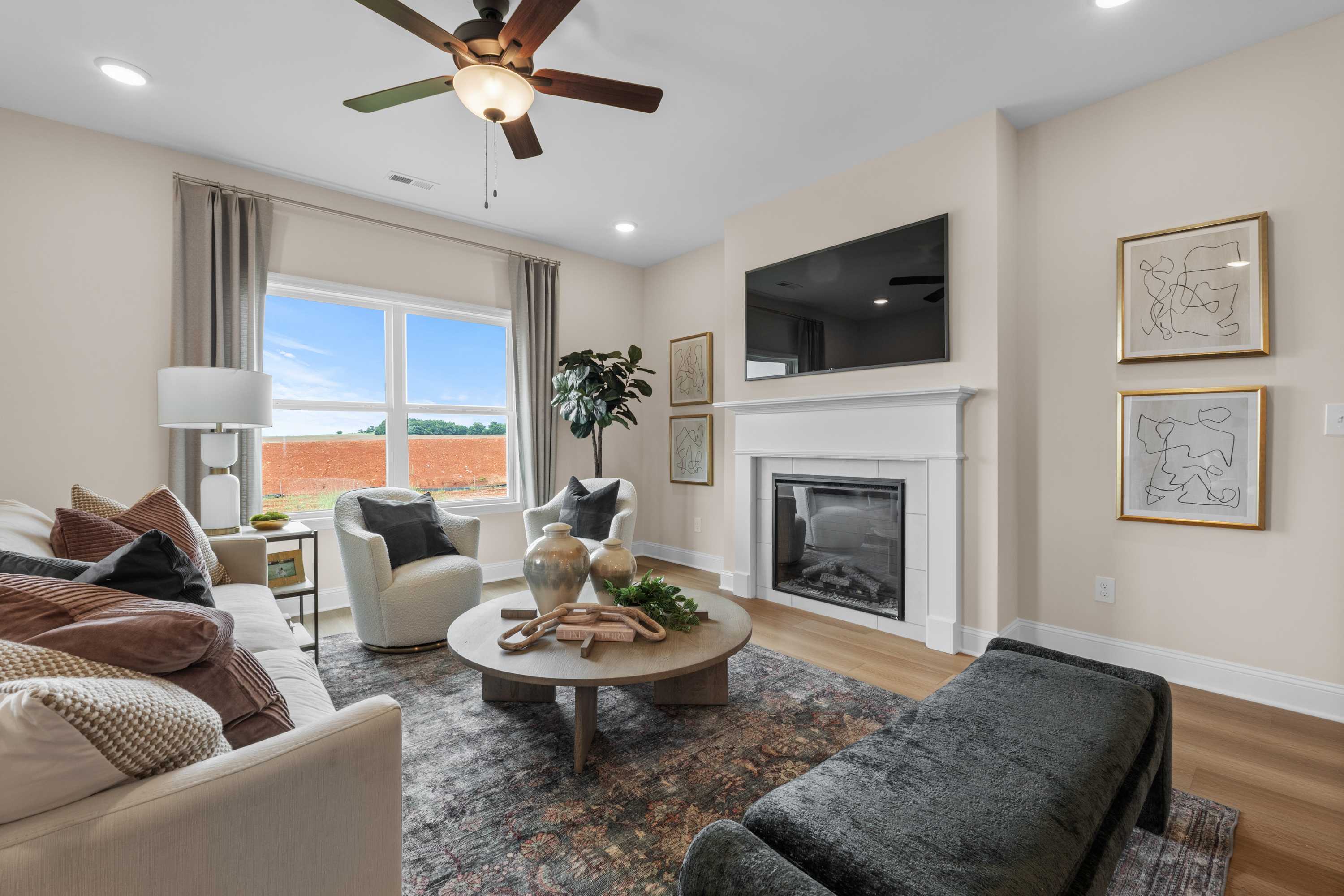 Cozy living room in The Daphne by Davidson Homes with white fireplace, beige sofa, large windows, and modern decor