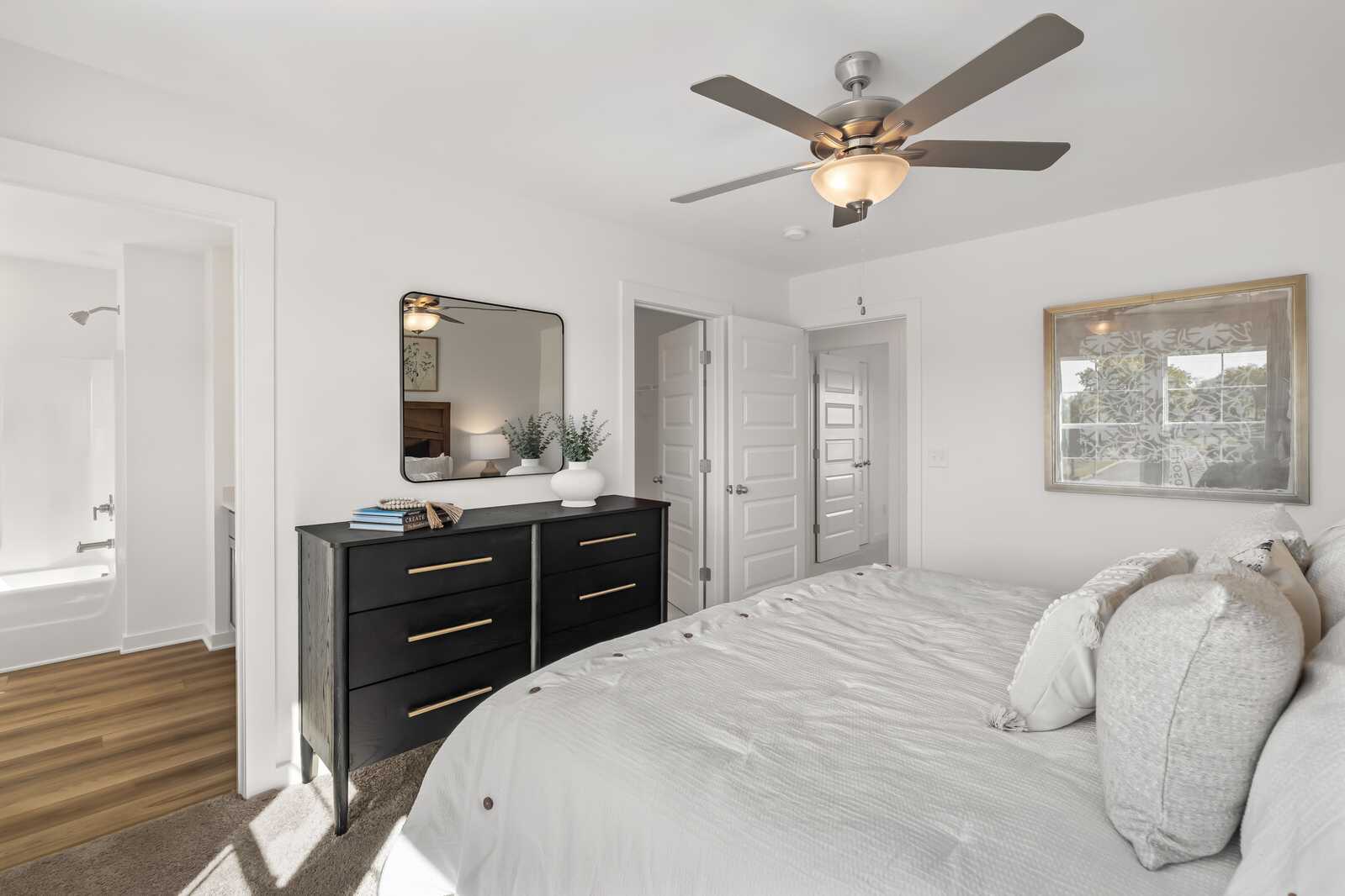 Spacious primary bedroom at The Towns at Red River in Gallatin TN with king bed, black dresser, ceiling fan, and en-suite bath