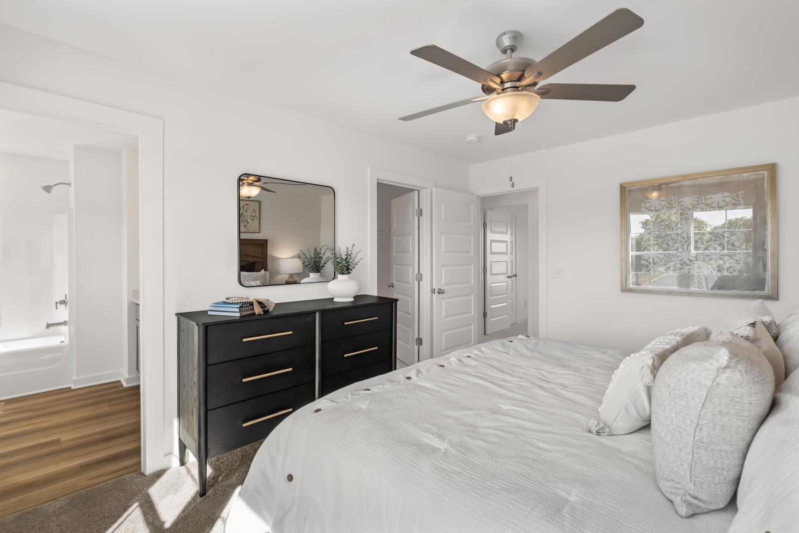 Spacious primary bedroom at The Towns at Red River in Gallatin TN with king bed, black dresser, ceiling fan, and en-suite bath