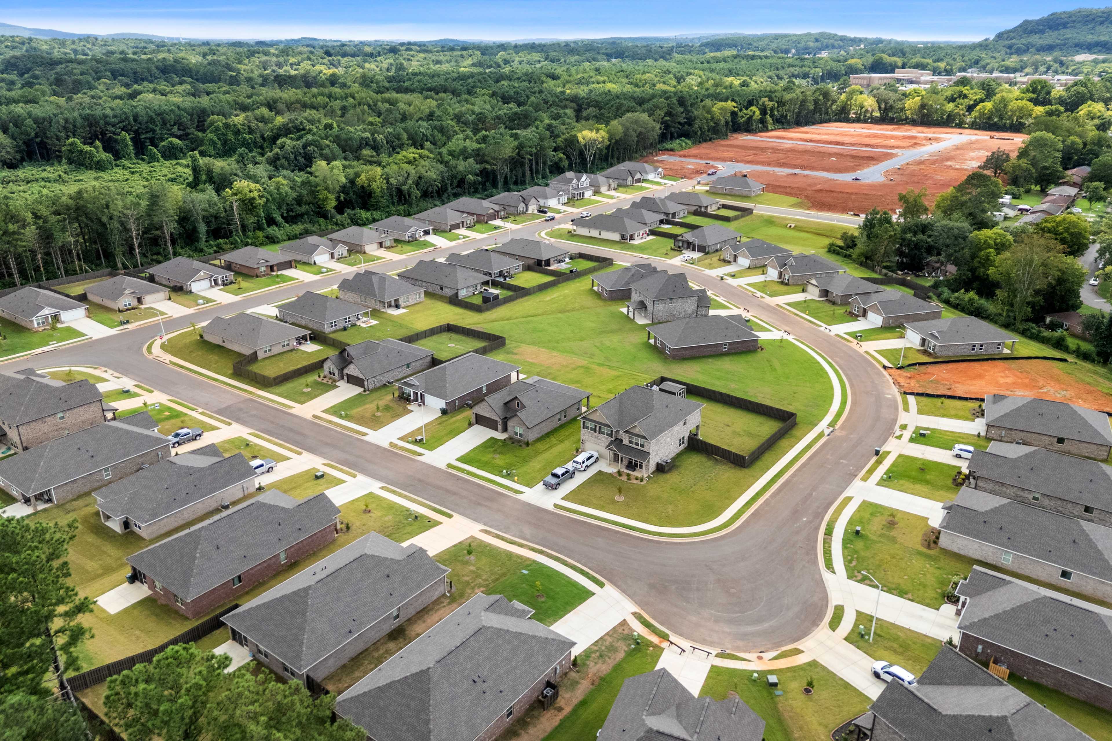 Aerial view of new homes in Blue Spring Huntsville AL by Davidson Homes with curving streets, green lawns and wooded surroundings