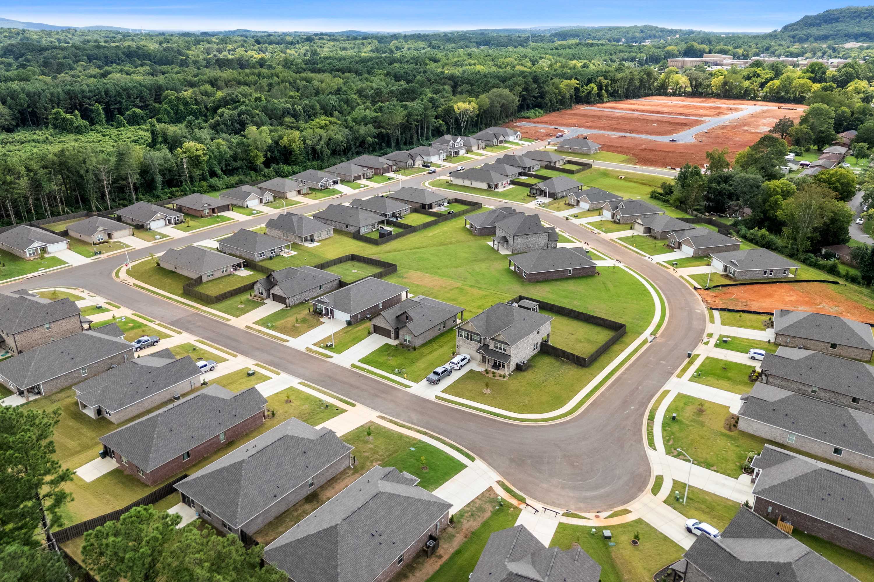 Aerial view of new homes in Blue Spring Huntsville AL by Davidson Homes with curving streets, green lawns and wooded surroundings