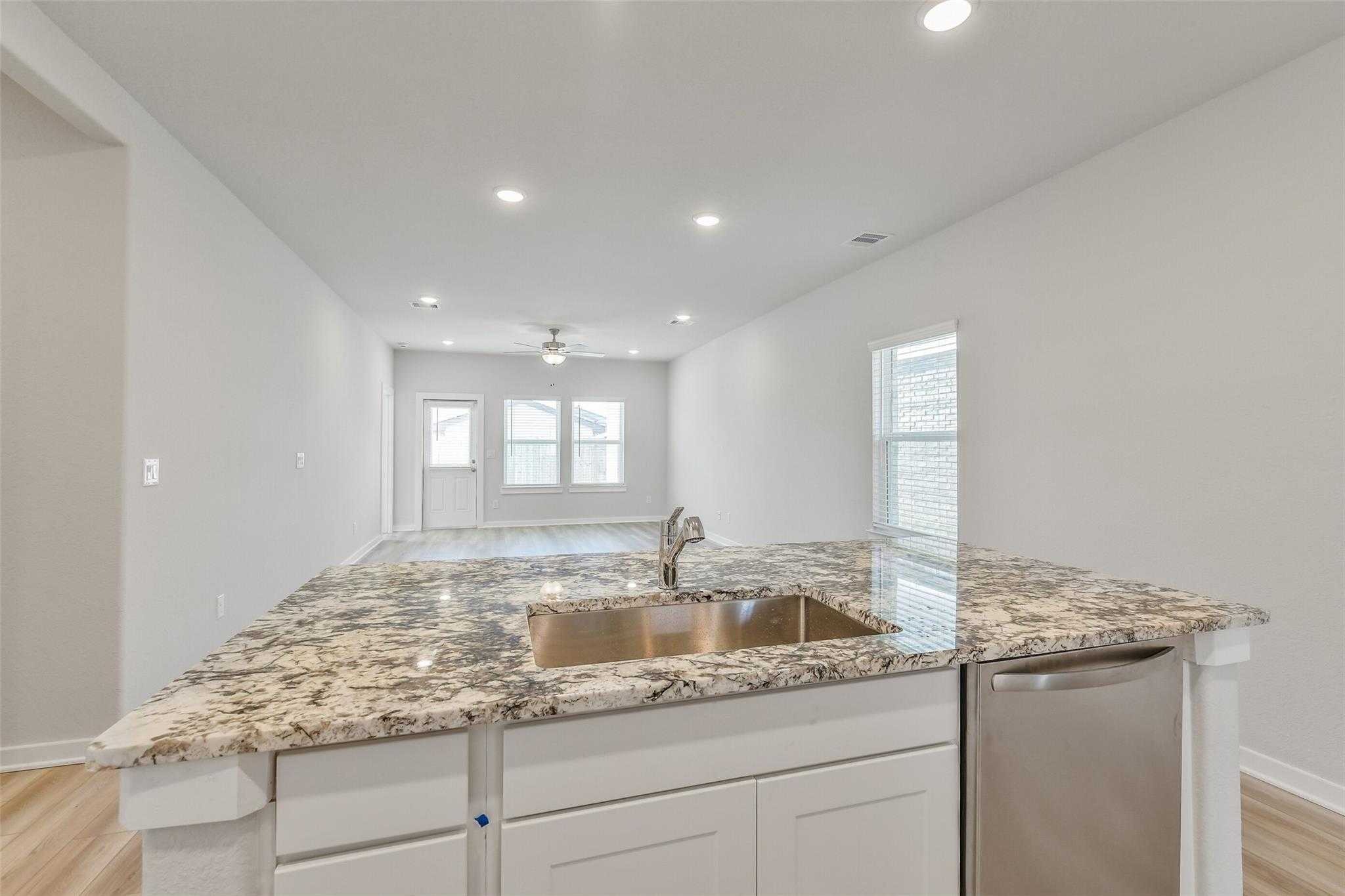 Modern open-concept kitchen with granite island, stainless sink, and white cabinets in The Rio Grande H by Davidson Homes, Magnolia TX