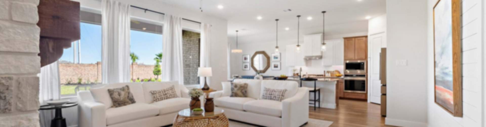 Spacious open-concept living room and kitchen in modern Conroe new home, white sofas, stone fireplace, large windows