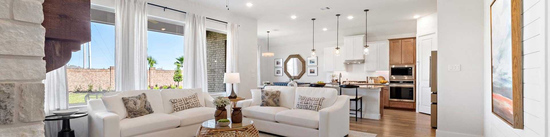Spacious open-concept living room and kitchen in modern Conroe new home, white sofas, stone fireplace, large windows