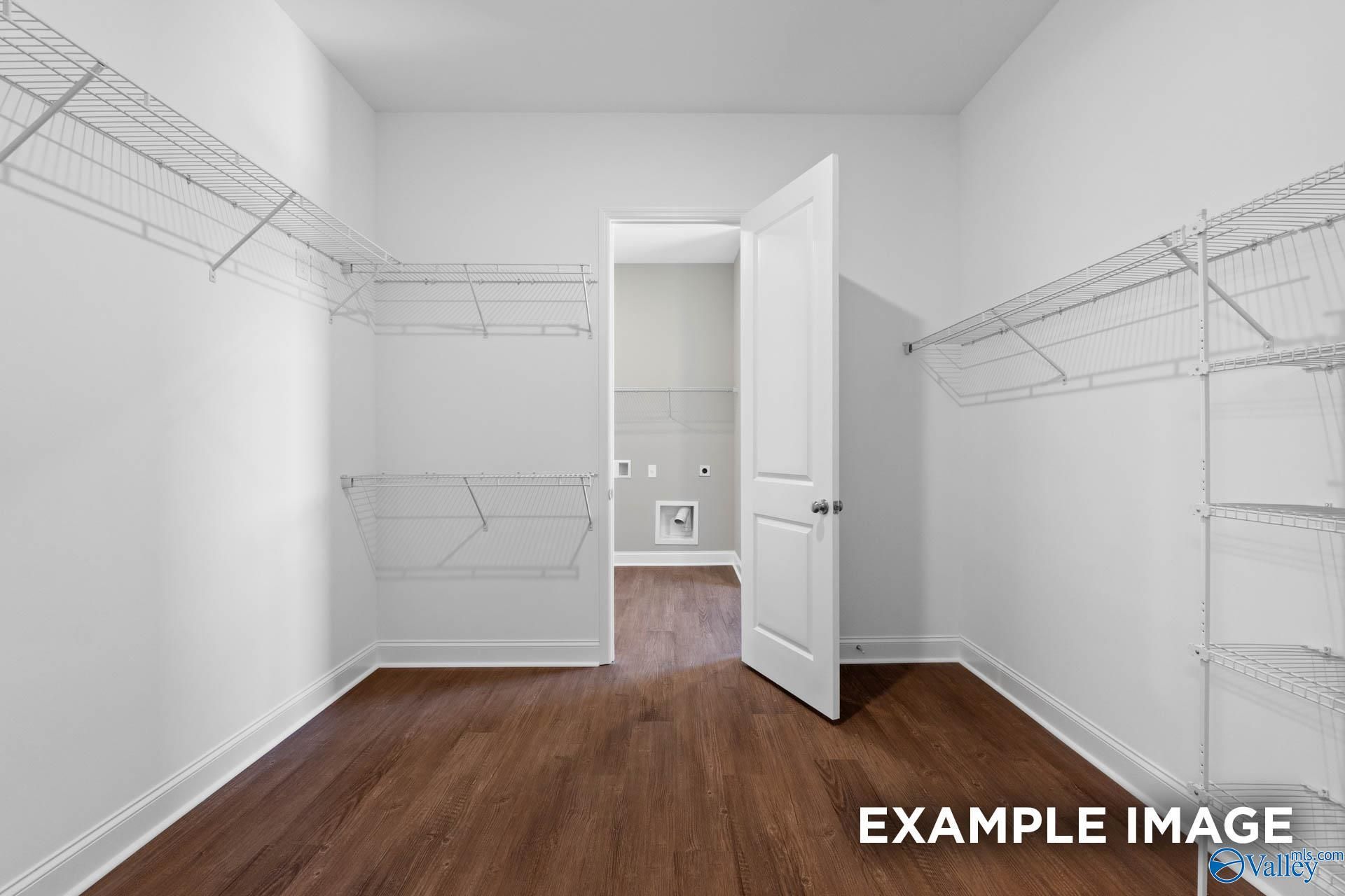 Spacious walk-in closet with white wire shelving, open bathroom door, and hardwood floors in Evermore Homes The Arcadia, Owens Cross Roads, Alabama