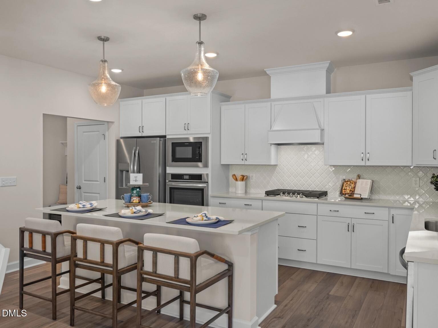 Modern white kitchen with large island, bar stools, stainless appliances, subway tile backsplash in Davidson Homes Hickory II D, Wake Forest, NC