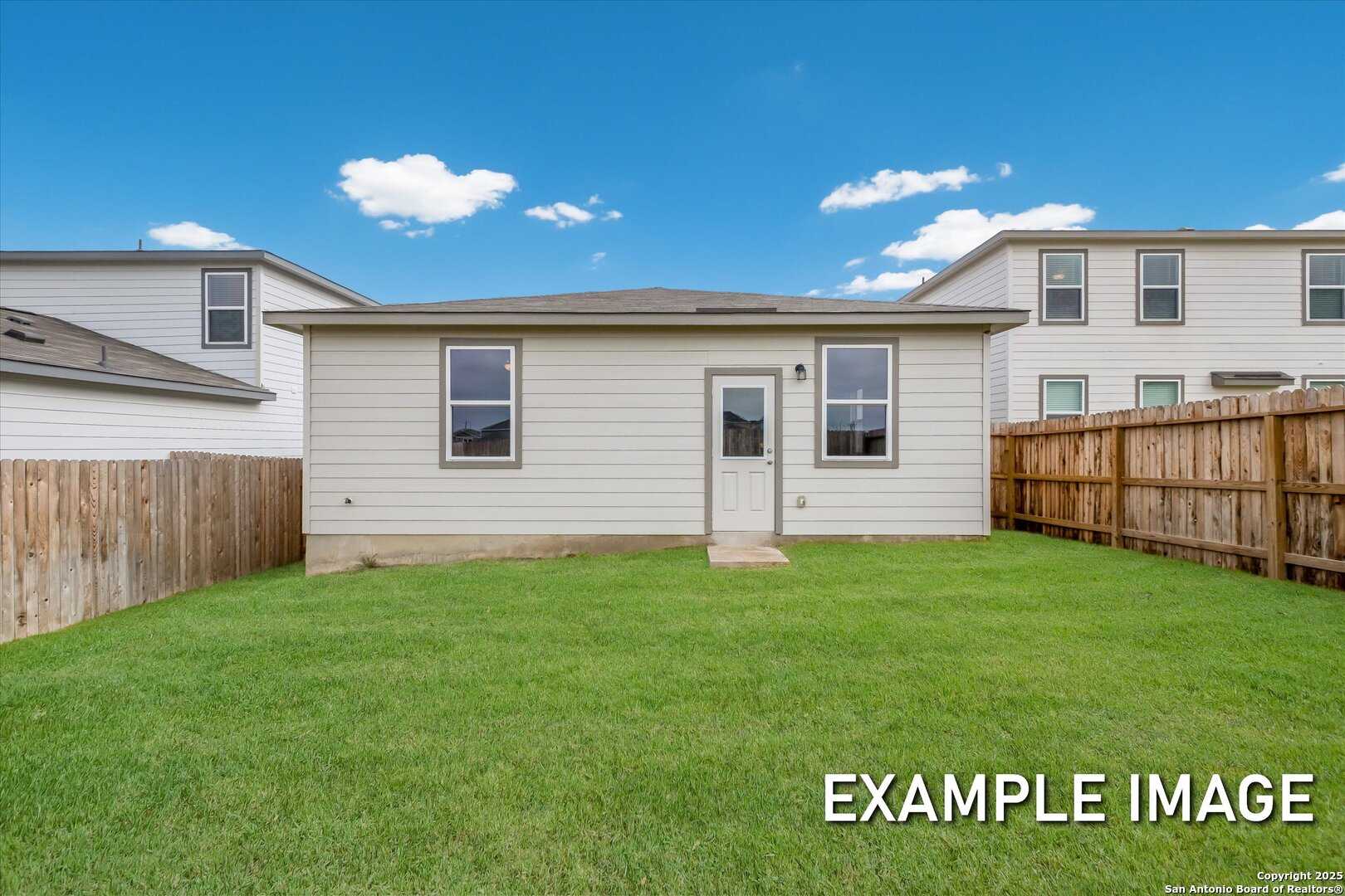 Backyard view of single-story 3-bedroom home with green lawn, wooden fence, and blue sky in Davidson Homes The Comal B, Agave, San Antonio