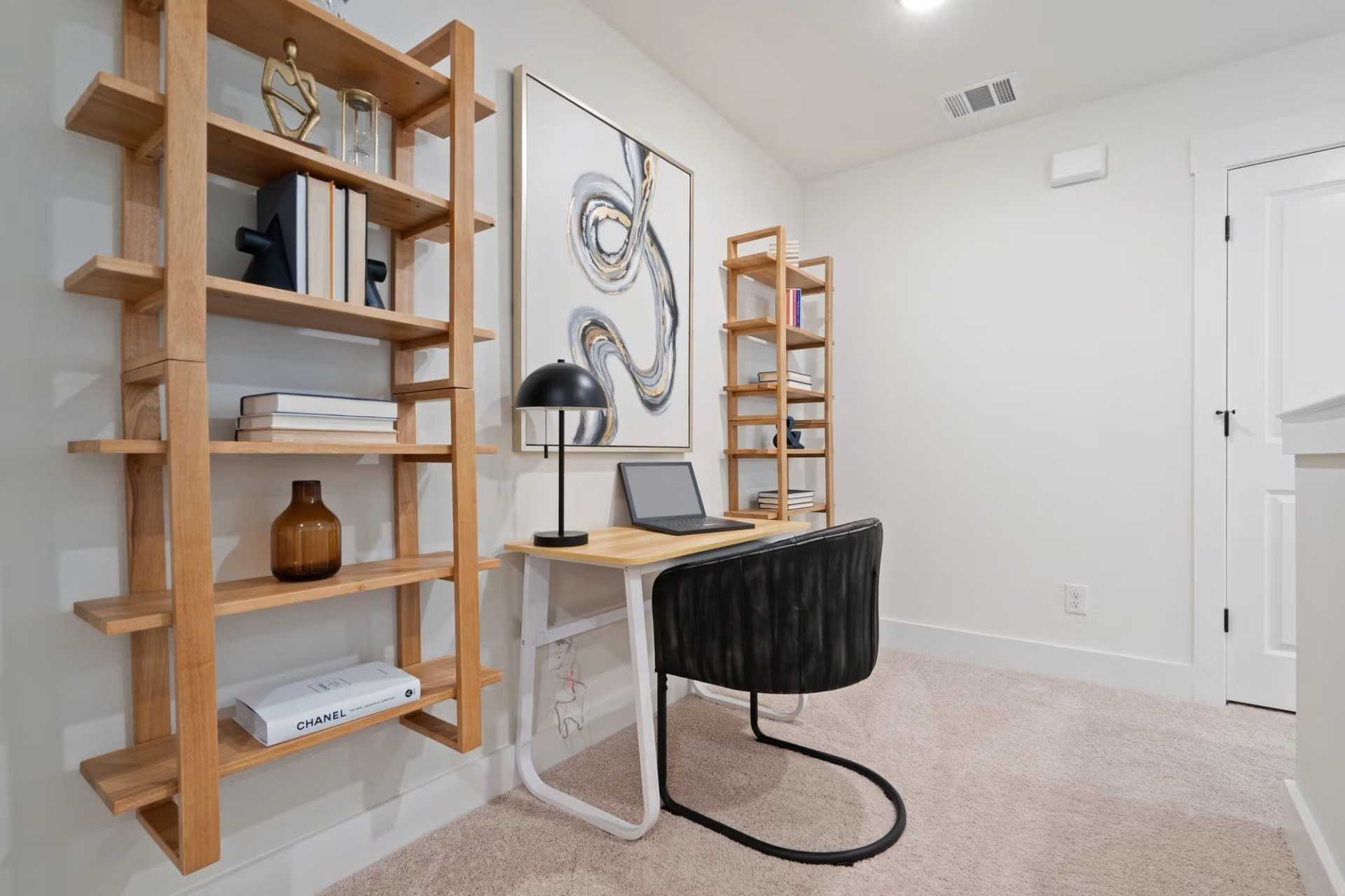Cozy home office with wooden bookshelves, abstract wall art, sleek desk, laptop and ergonomic chair in Davidson Homes The Wake D, Wylie, Texas