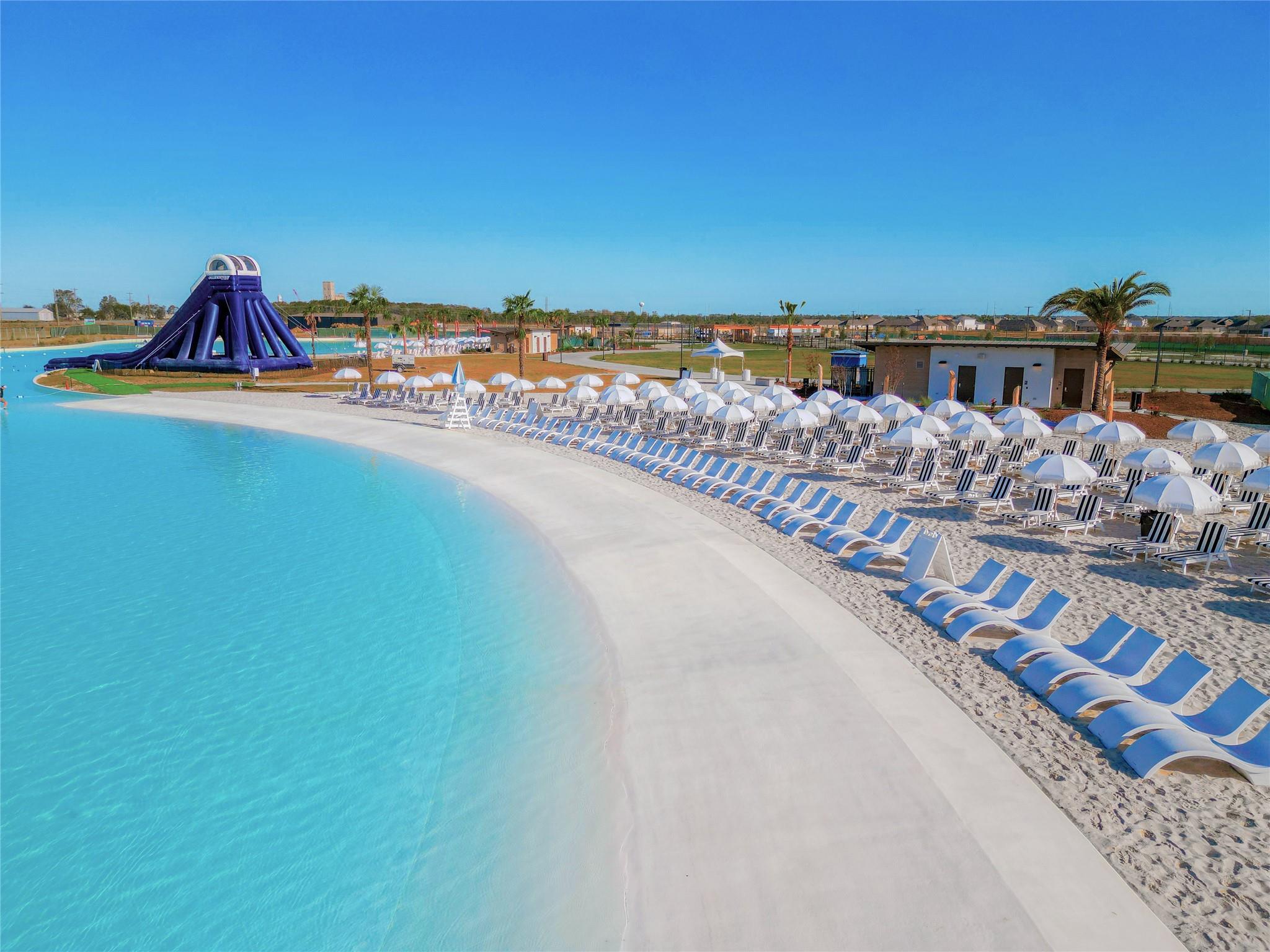 Crystal clear lagoon with beach chairs, umbrellas, and water slide at River Ranch Meadows in Dayton, Texas.