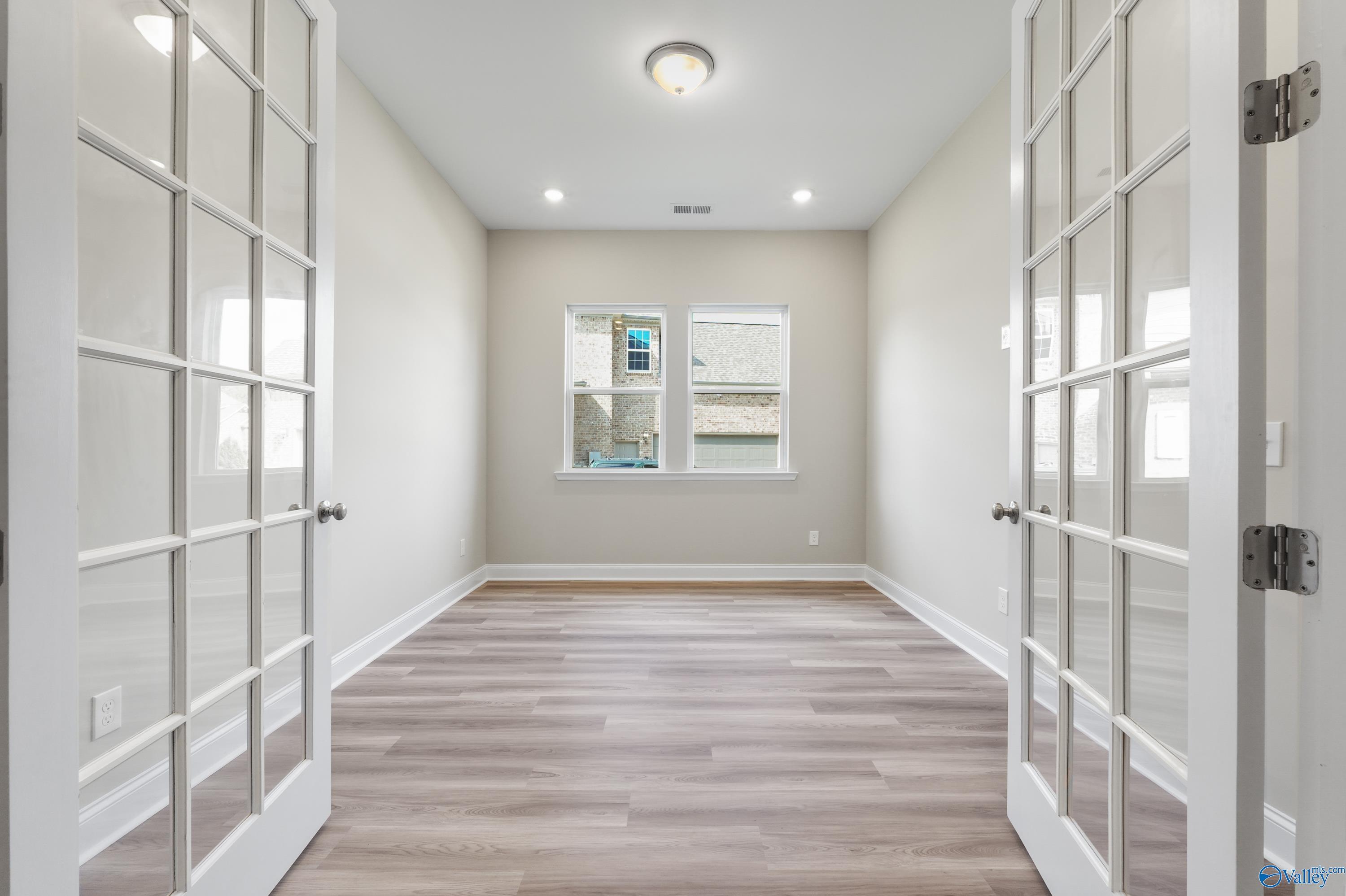 Bright empty room with beige walls, light hardwood floors, French doors, and large windows in Evermore Homes The Haven, Owens Cross Roads