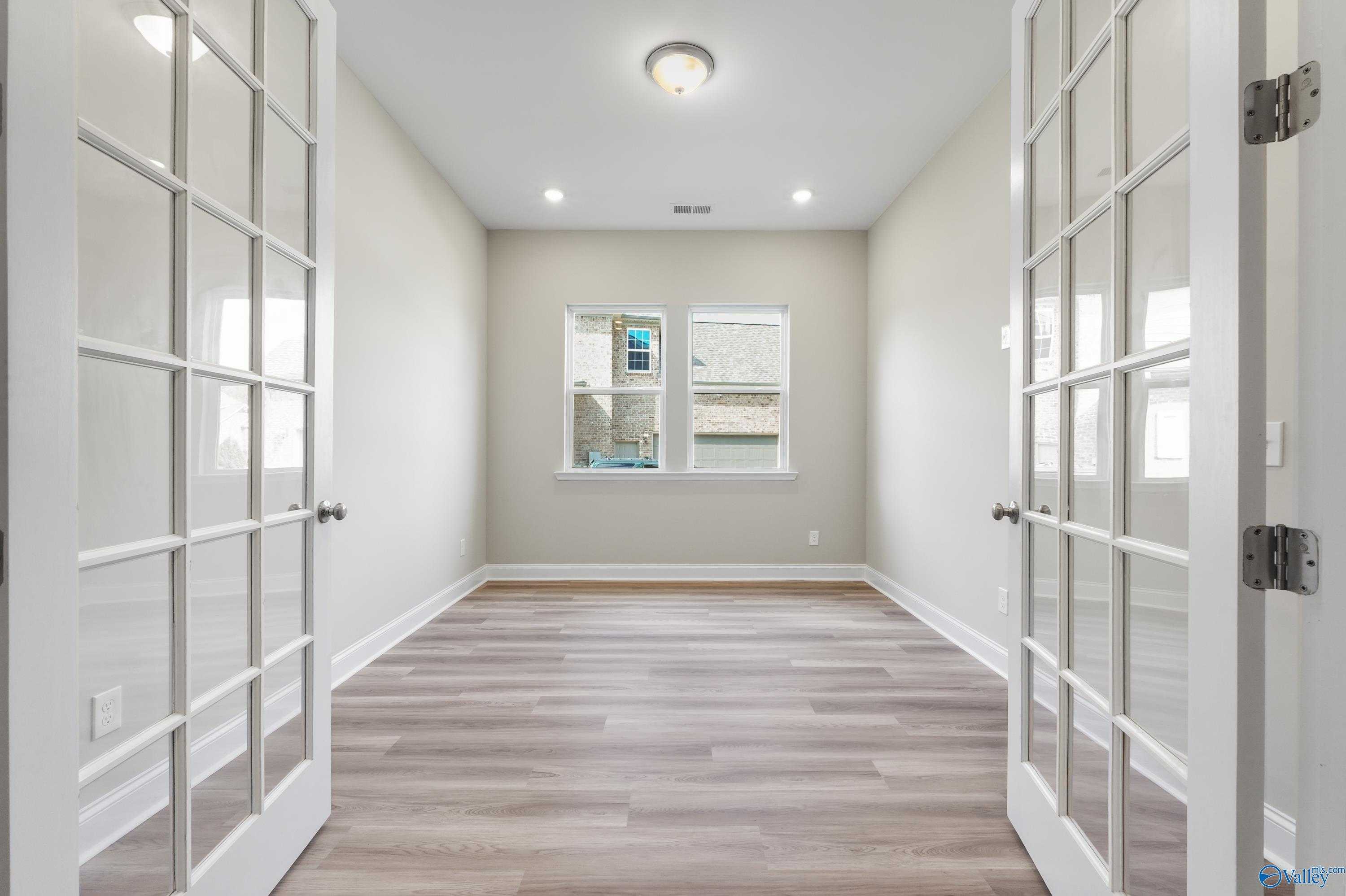 Bright home study with open French doors, beige walls, and window overlooking outdoors in Evermore Homes The Haven, Owens Cross Roads, Alabama