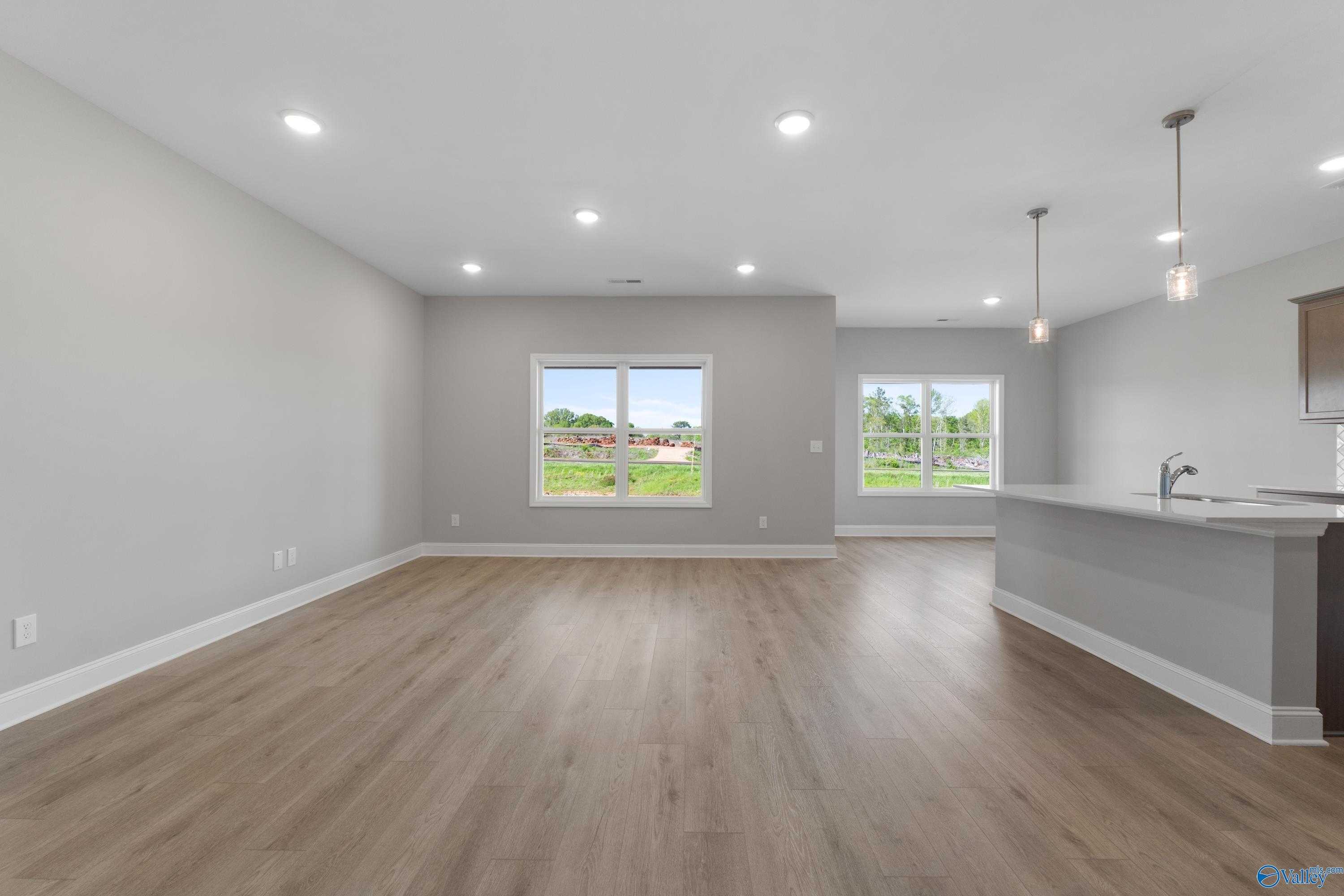 Open-concept living room and kitchen with hardwood floors, gray island, and yard-view windows in The Asheville C, Athens, Alabama