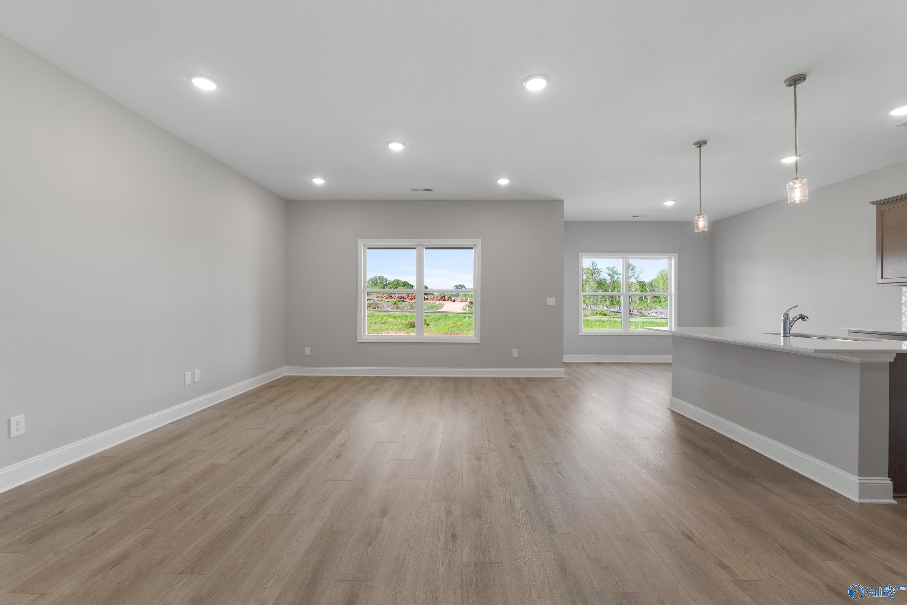 Open-concept living room and kitchen with hardwood floors, gray island, and yard-view windows in The Asheville C, Athens, Alabama