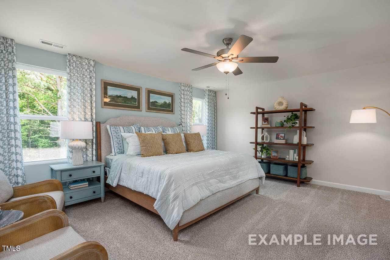 Elegant master bedroom with king bed, ceiling fan, large windows, and built-in bookshelf in Davidson Homes The Willow G, Angier, NC