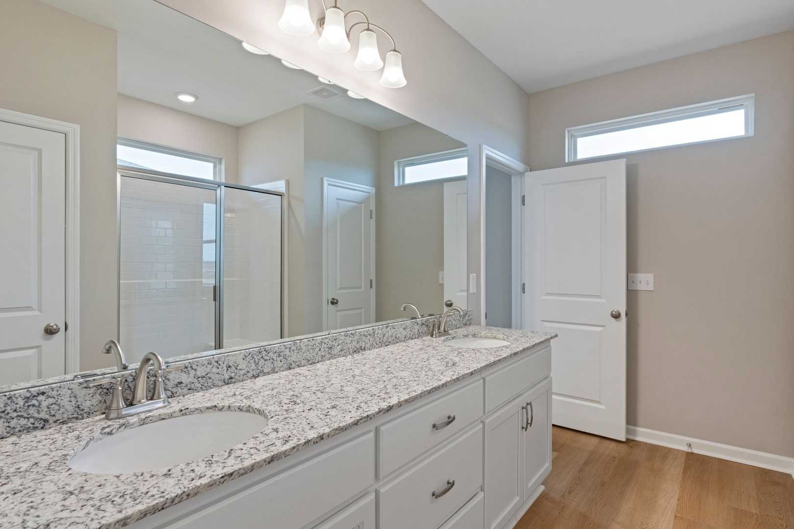 Spacious master bathroom in The Stella with double granite vanity, large mirrors, walk-in shower, and neutral tones