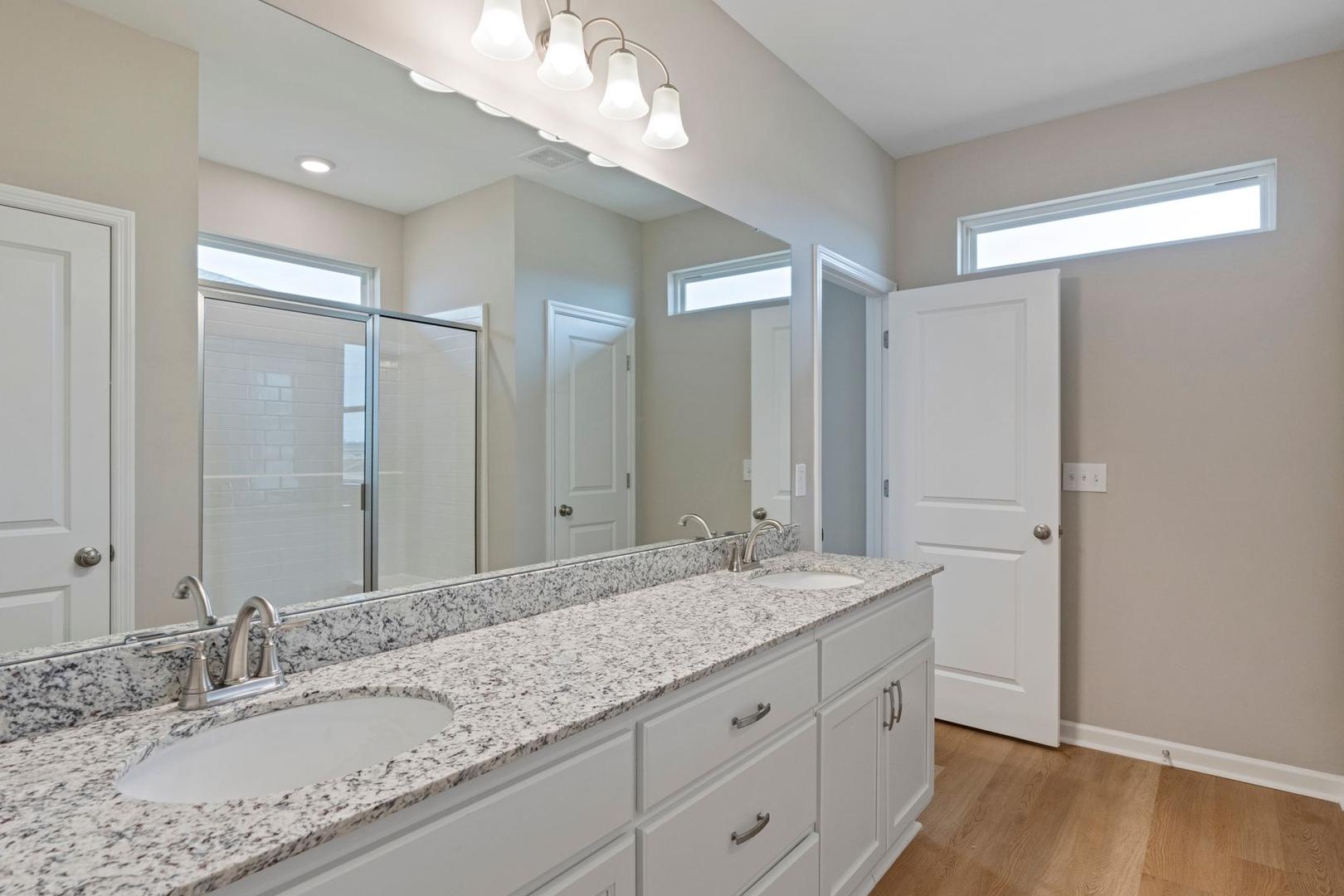 Spacious master bathroom in The Stella A with double granite vanity, large mirror, walk-in shower, beige walls