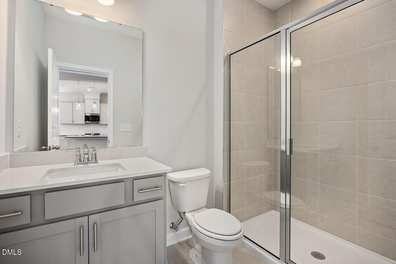 Modern primary bathroom with gray vanity, single sink, toilet, and glass-enclosed shower in Davidson Homes The Willow G, Angier, NC