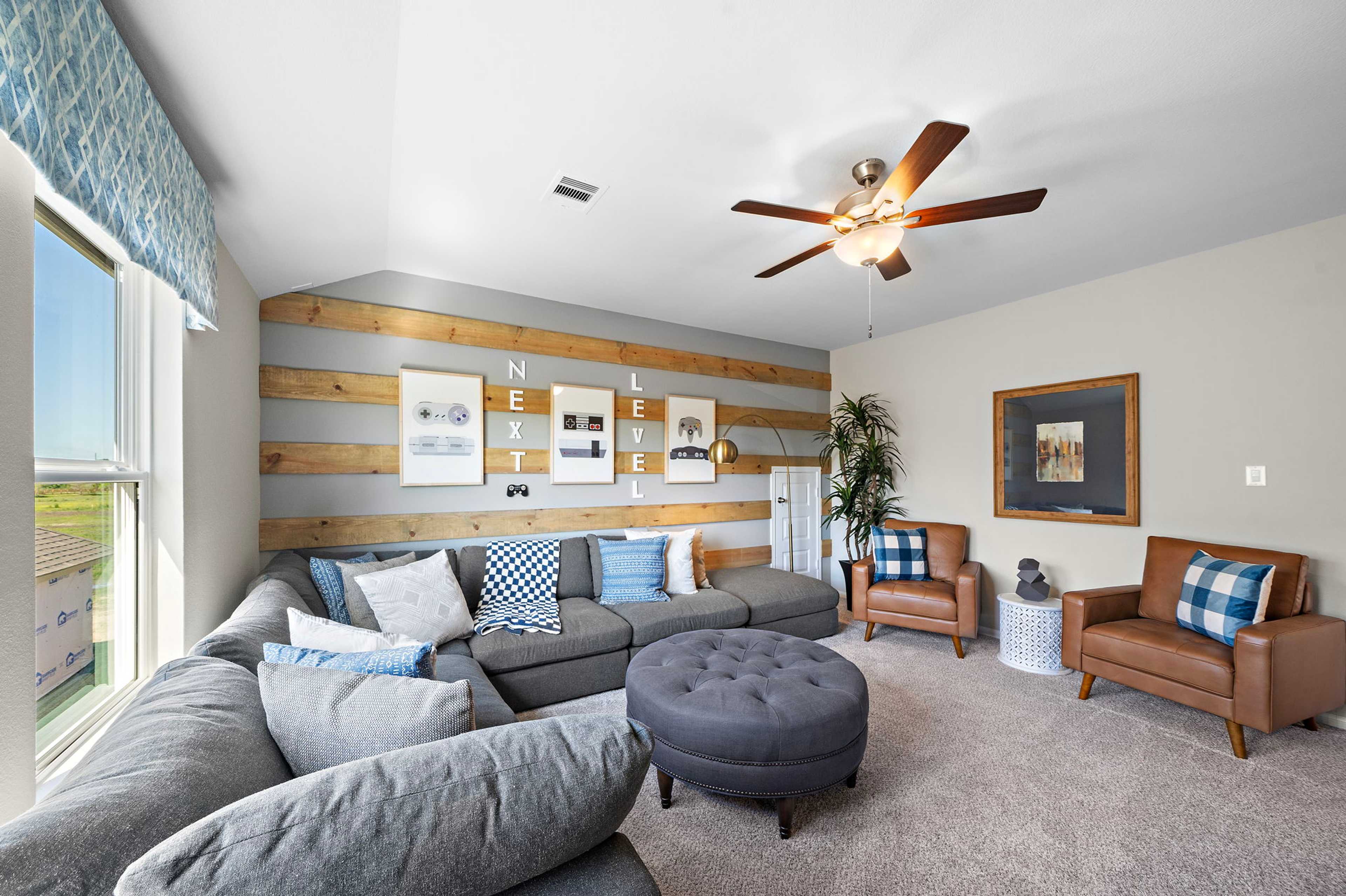 Cozy media room at Emberly in Beasley Texas by Davidson Homes with gray L-shaped sofa, shiplap accent wall, and ceiling fan