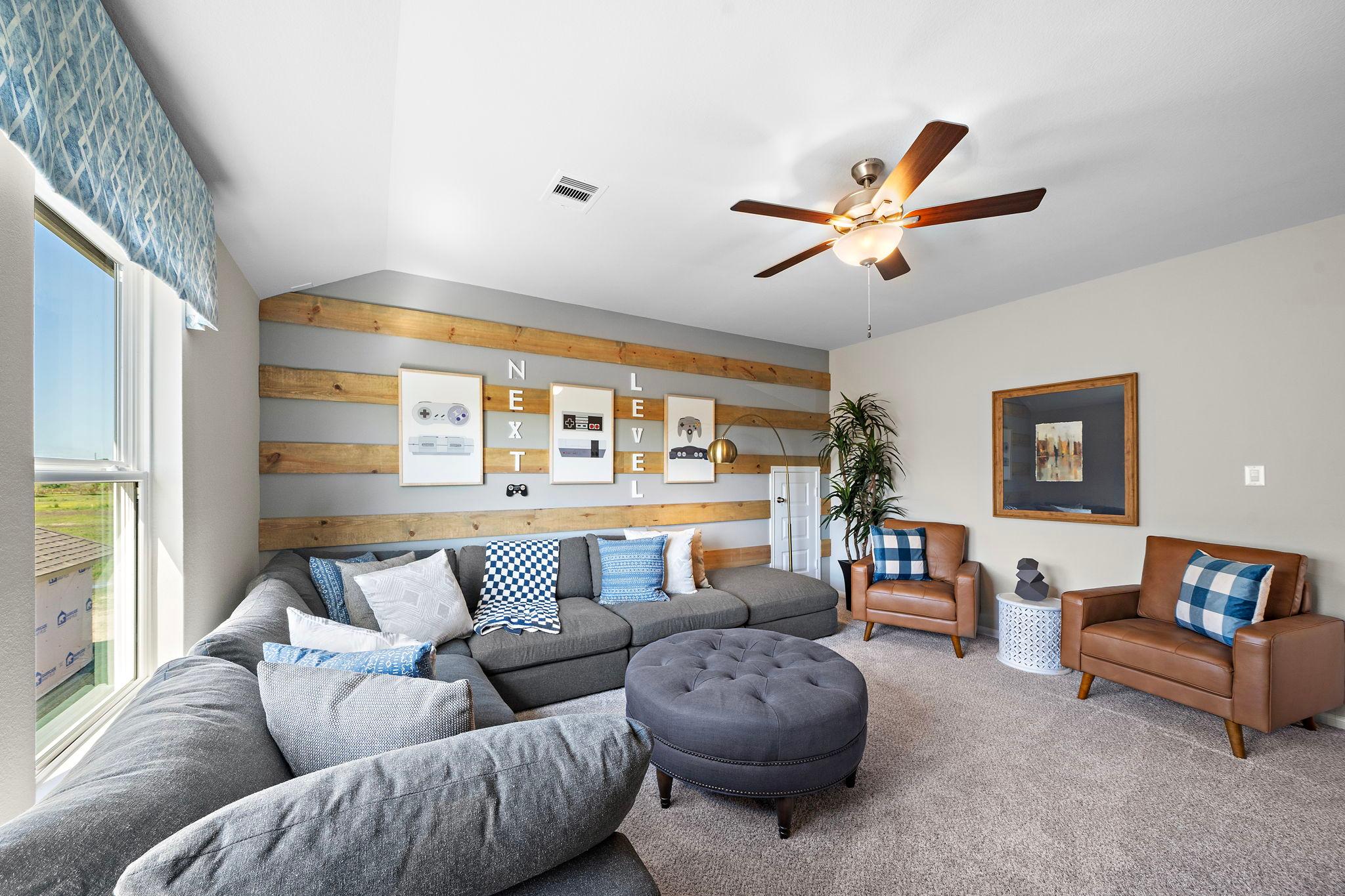 Cozy media room at Emberly in Beasley Texas by Davidson Homes with gray L-shaped sofa, shiplap accent wall, and ceiling fan