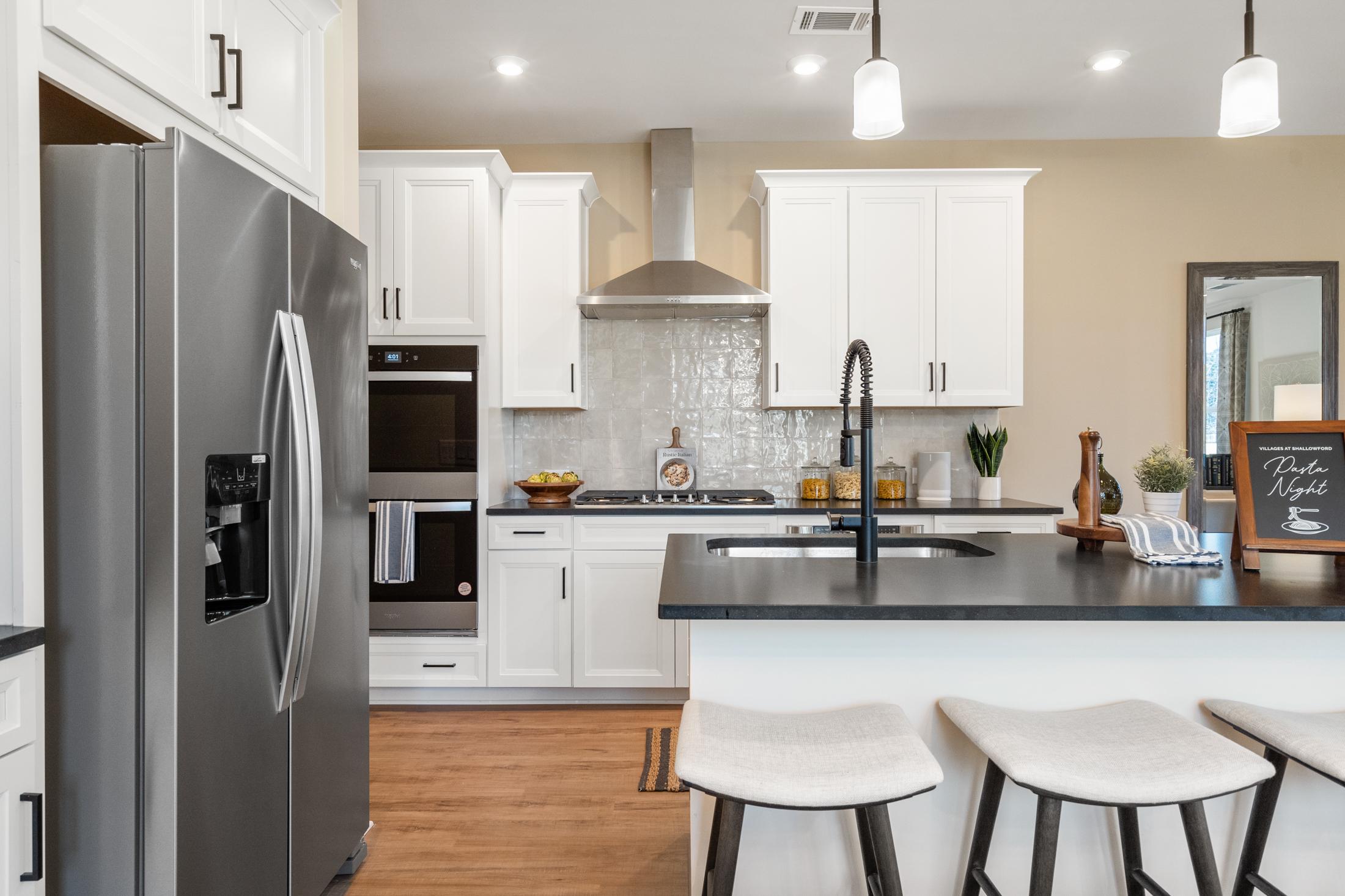 Spacious modern kitchen in The Marion A with white shaker cabinets, stainless steel appliances, black island, and pendant lights