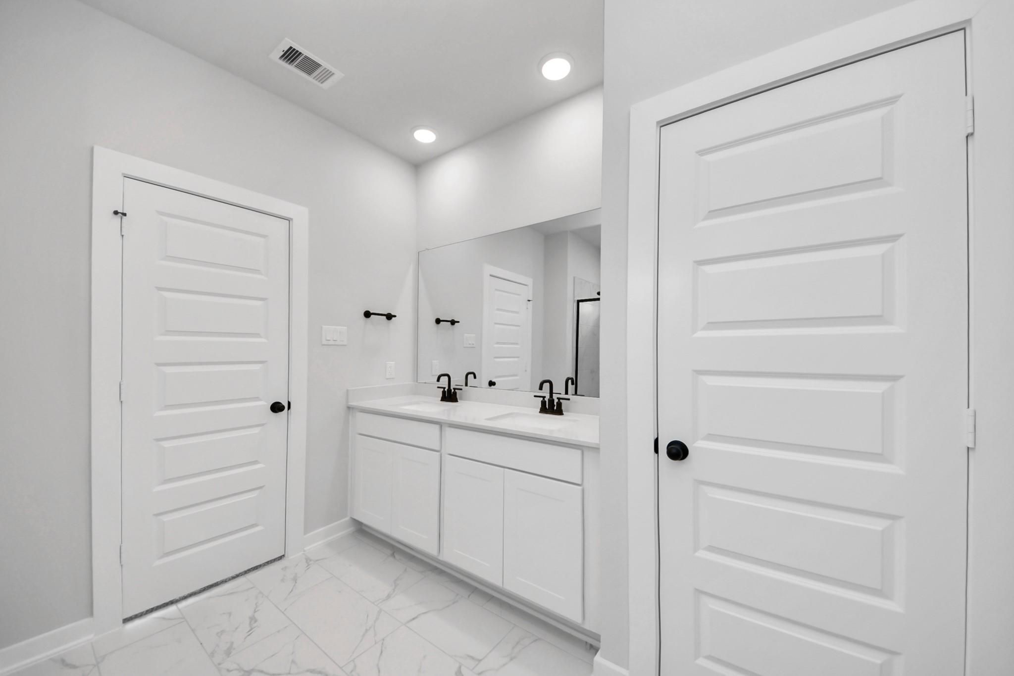 Modern bathroom with double vanity, white cabinets, and marble-look tile in The Everett C floor plan, Dayton, Texas.