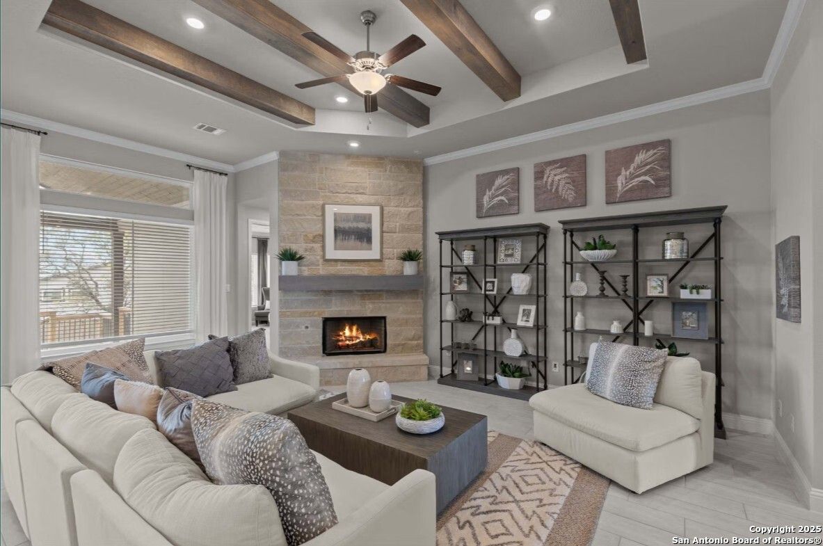 Cozy living room with stone fireplace, wooden beams, ceiling fan, and beige sofa in Davidson Homes The Garner B, Ladera, San Antonio