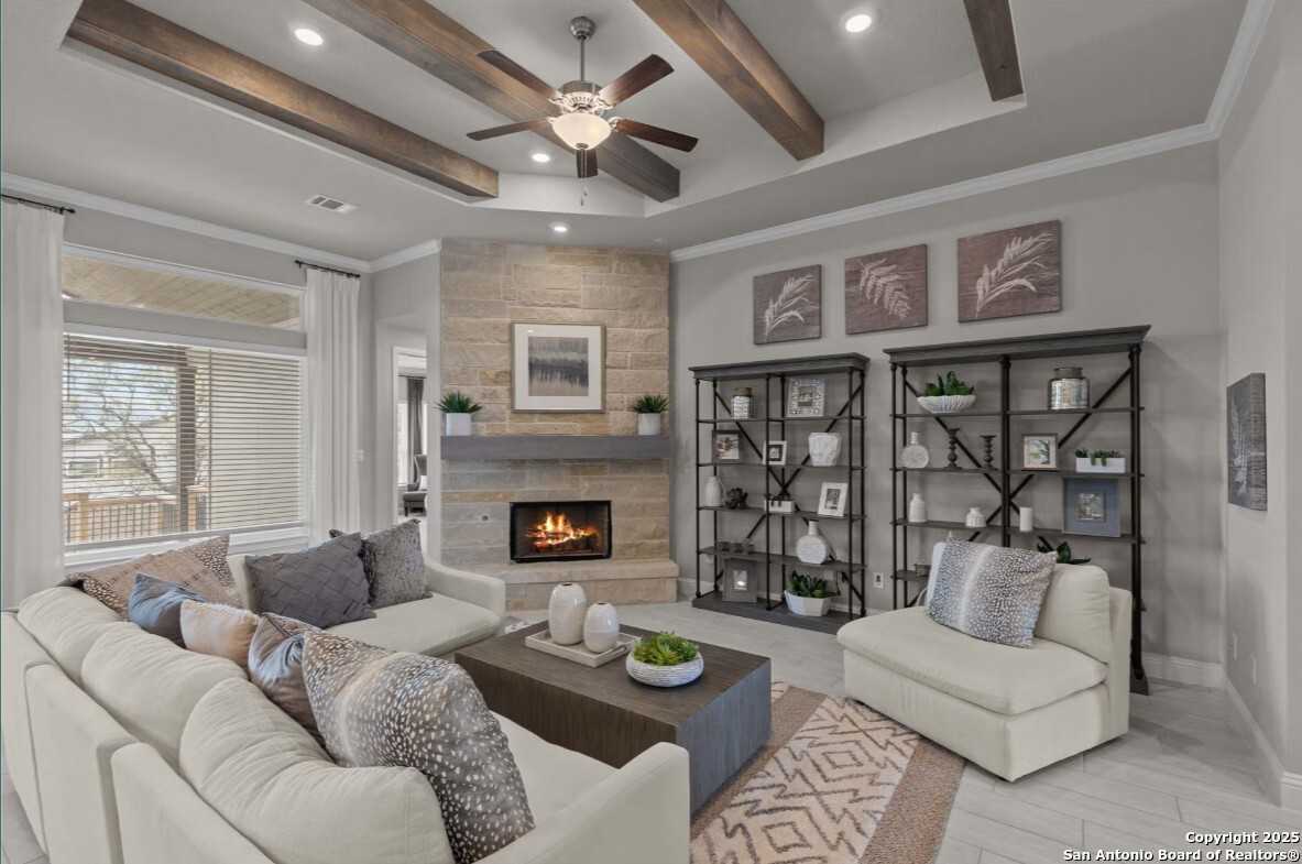 Cozy living room with stone fireplace, wooden beams, ceiling fan, and beige sofa in Davidson Homes The Garner B, Ladera, San Antonio