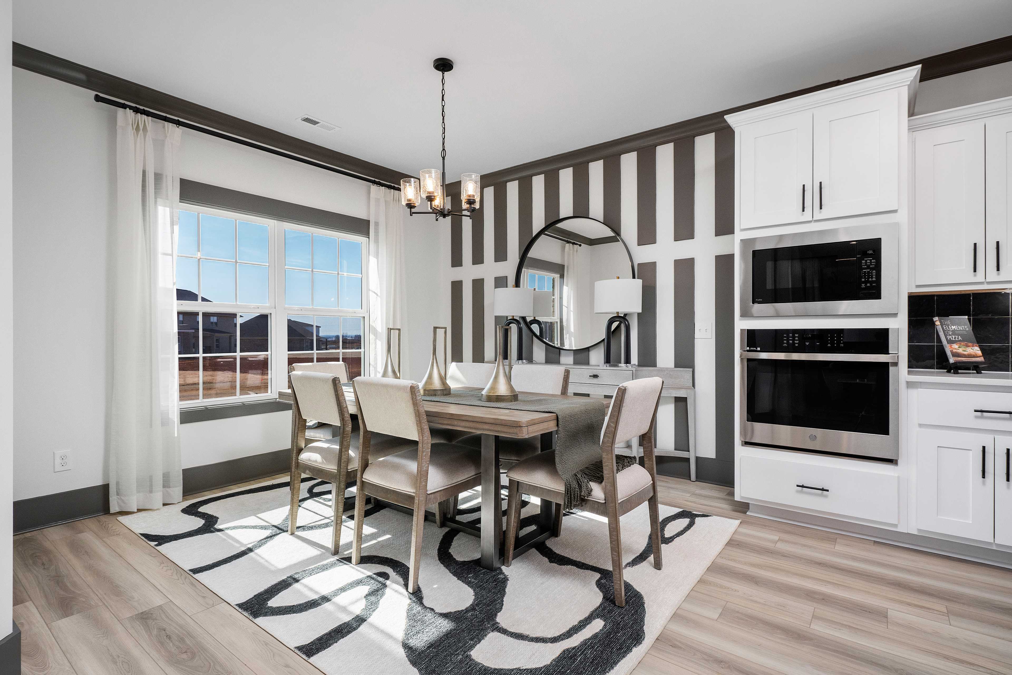 Elegant dining room at Barnett's Crossing in Madison, AL with wooden table, chandelier, striped accent wall, and open white kitchen