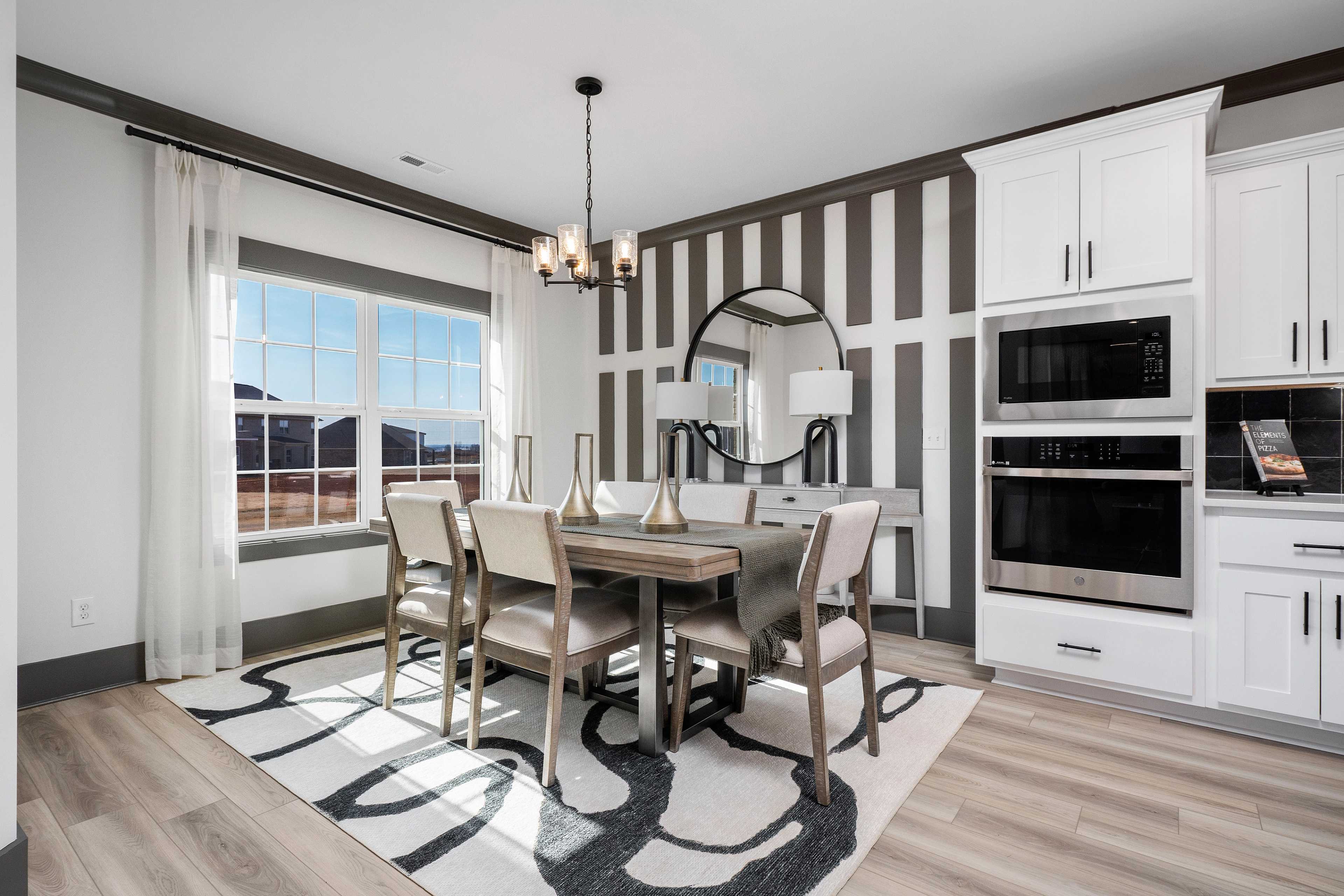 Elegant dining room at Barnett's Crossing in Madison, AL with wooden table, chandelier, striped accent wall, and open white kitchen